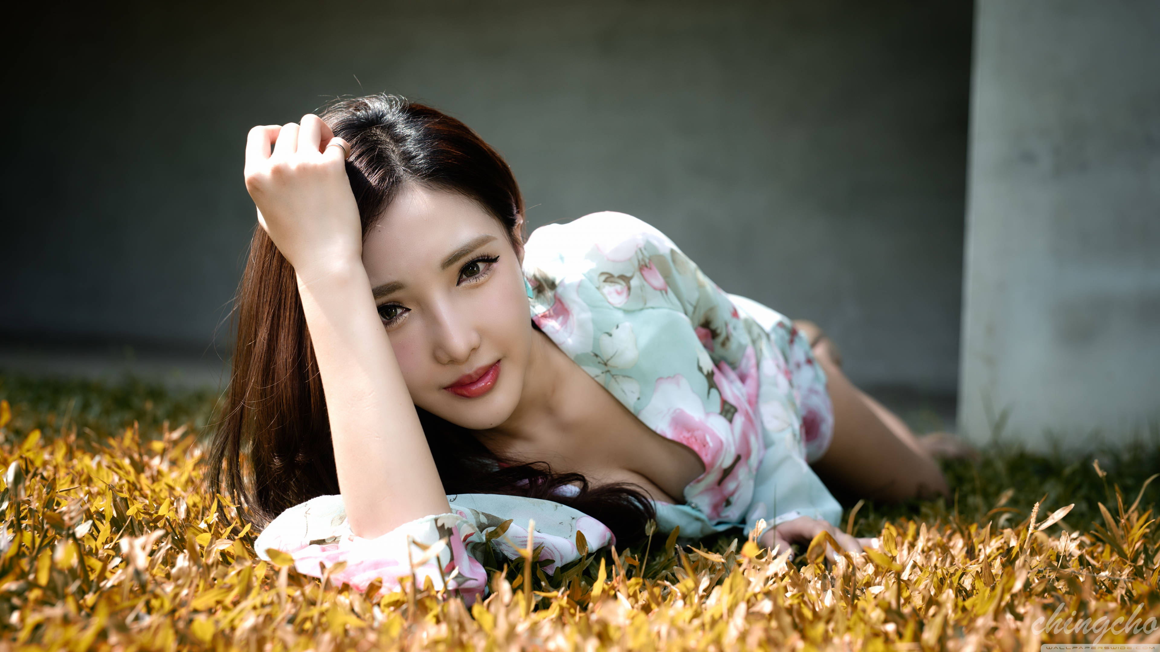 女孩 桌布 壁紙 — 一位身穿花卉連衣裙的女性躺在金色草地上，一隻手放在頭附近，溫柔地凝視著相機。