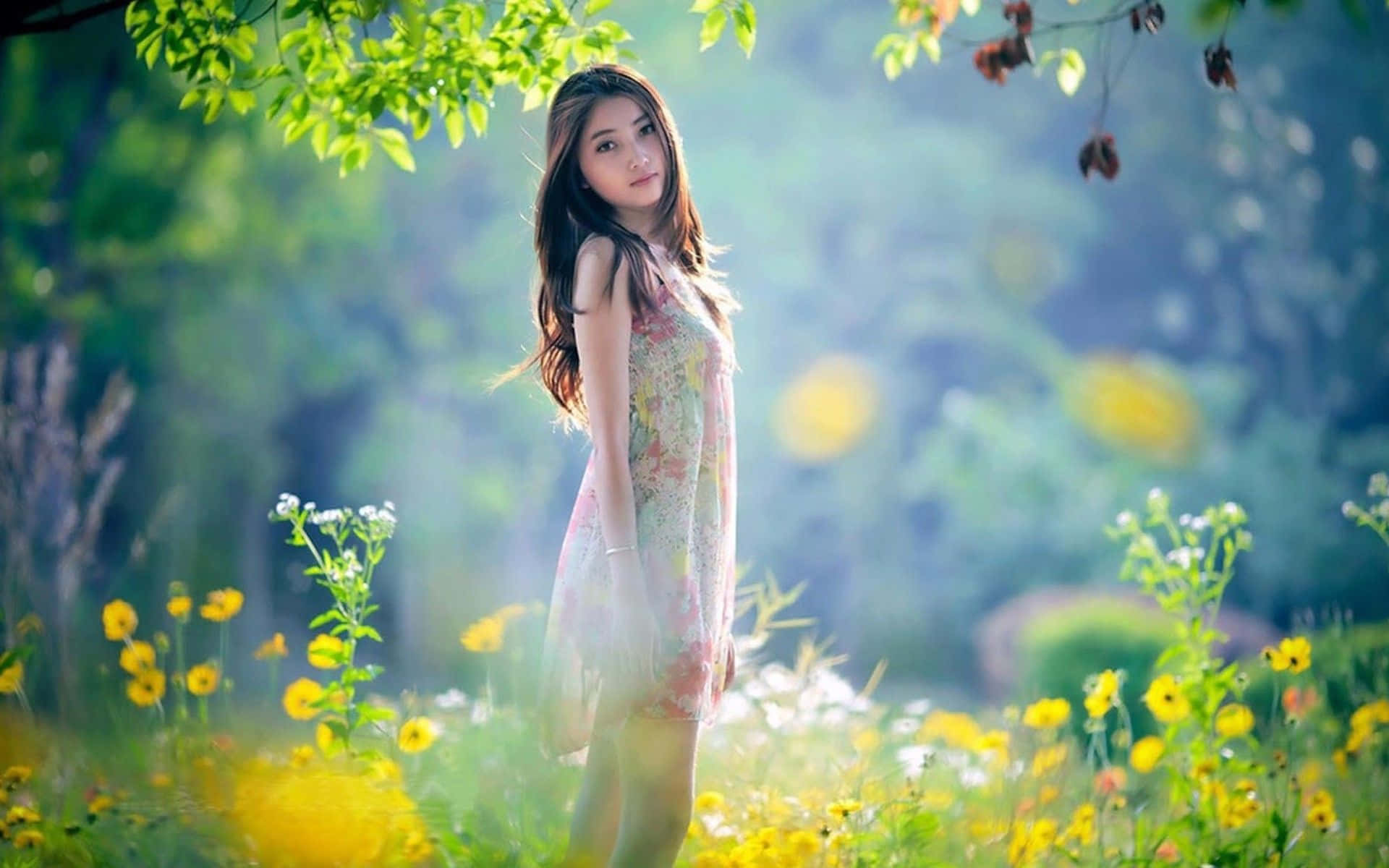 Beautiful Photography 桌布 壁紙 — 一位身穿花卉連衣裙的年輕女子，在斑駁的綠色樹葉下，優雅地站在陽光普照的黃色野花叢中。