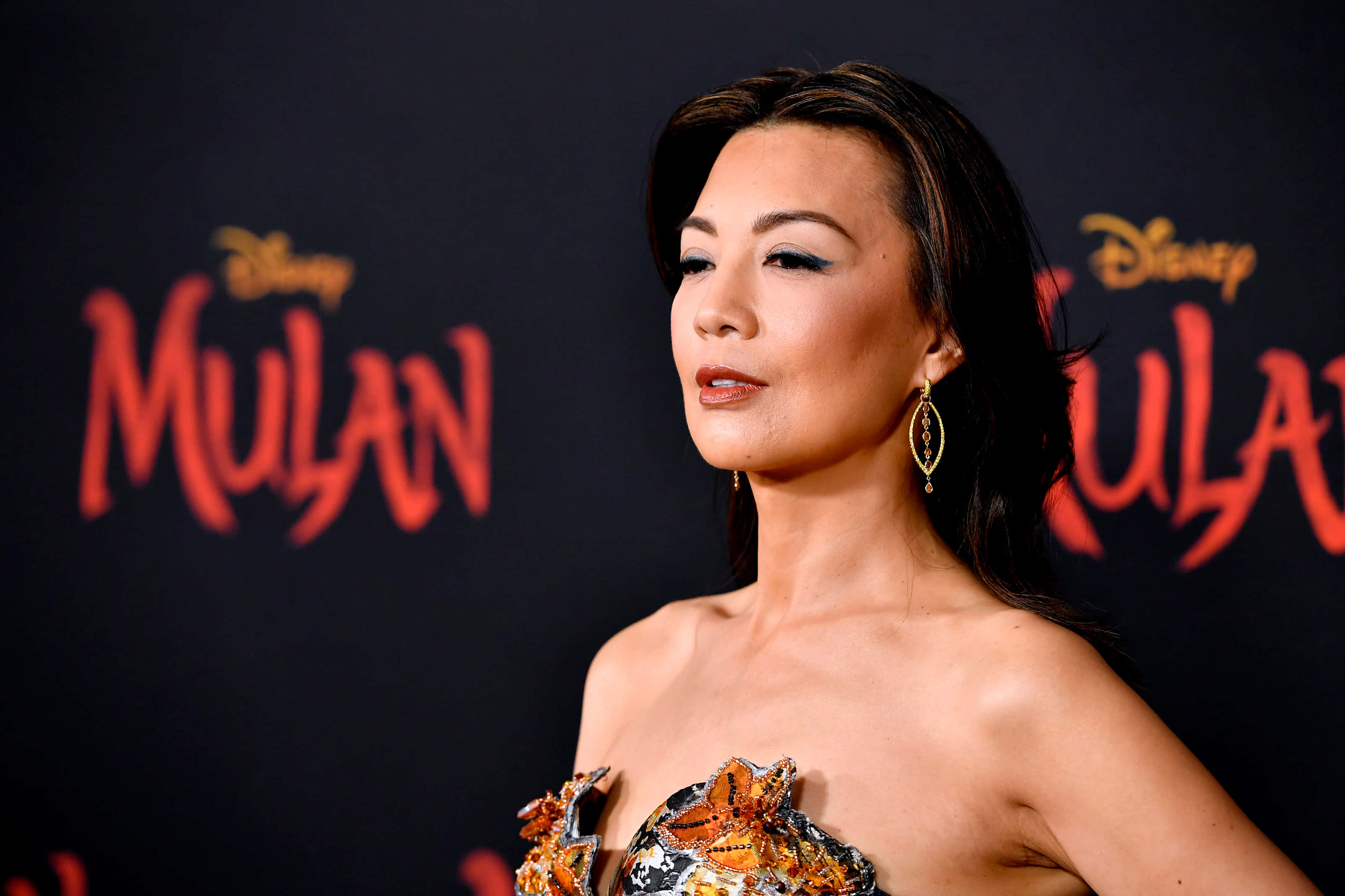 Ming Na Wen 桌布 壁紙 — 一位身穿華麗無肩帶禮服的女士在迪士尼花木蘭首映禮上，以醒目的紅色標誌背景擺姿勢。