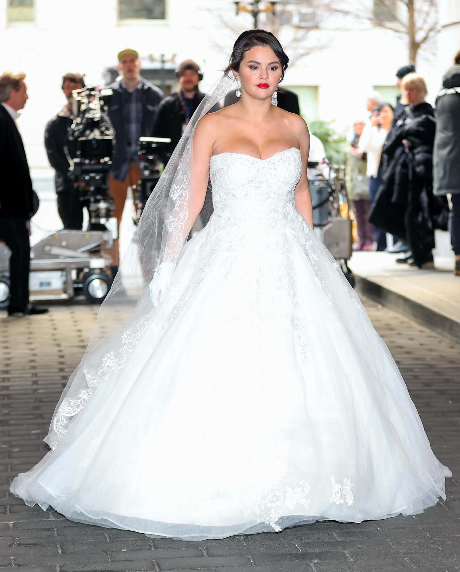 Bride's Dress 桌布 壁紙 — 一位身穿華麗白色婚紗、帶有蕾絲細節和飄逸頭紗的女性，自信地走在鵝卵石街道上。