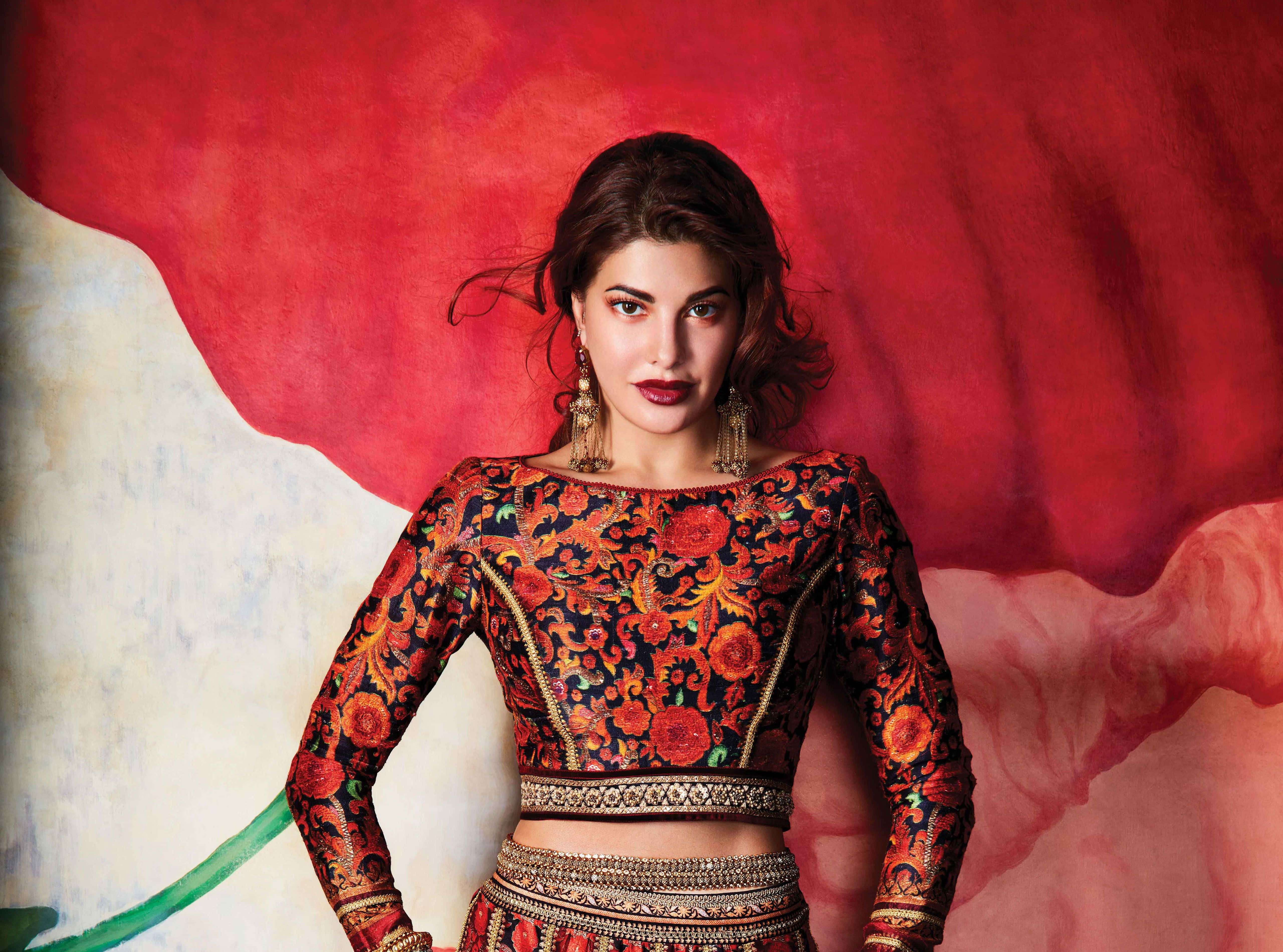 Jacqueline Fernandez 桌布 壁紙 — 一位身穿華麗紅色花卉服飾的女性，自信地站在大膽的紅白抽象背景前。