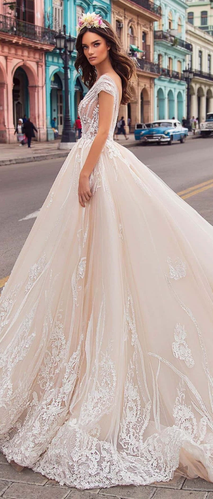 Wedding Dress 桌布 壁紙 — 一位身穿華麗象牙白婚紗、頭戴花卉頭飾的女性，站在充滿活力的殖民風格街道上，兩旁是粉彩建築和復古汽車。