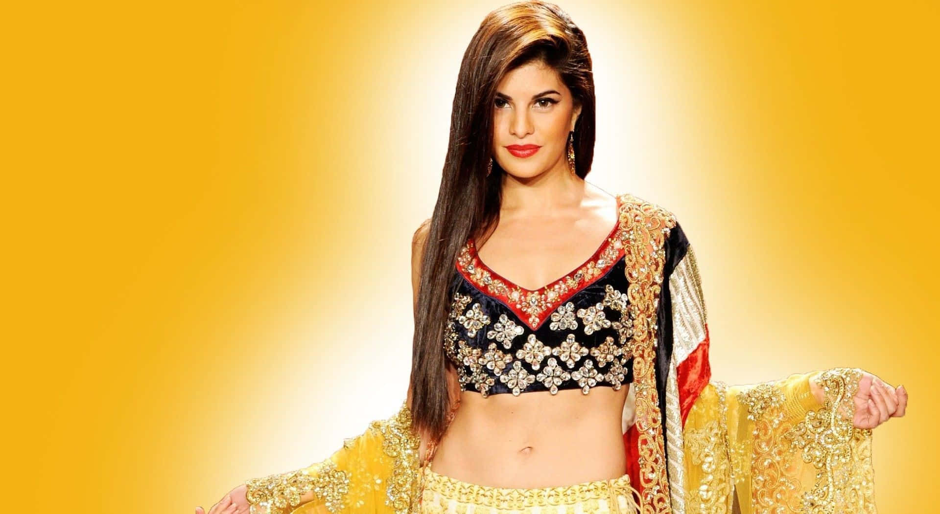 Jacqueline Fernandez 桌布 壁紙 — 一位身穿華麗金色和黑色傳統服飾的女性，在耀眼的黃色漸變背景前自信地擺姿勢。