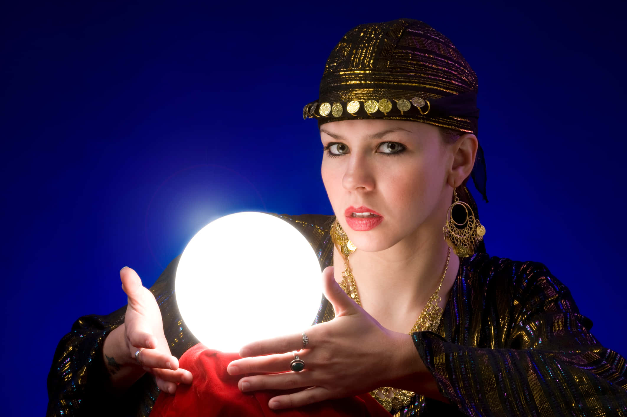 Fortune Teller 桌布 壁紙 — 一位身穿華麗金色和黑色服飾的女性，在深藍色背景前手持發光的水晶球。