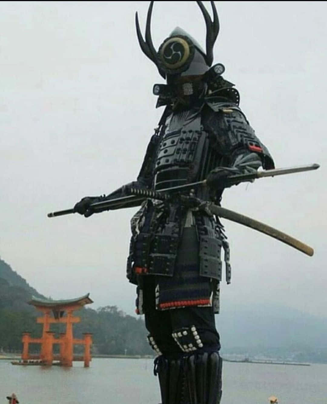 Ronin 桌布 壁紙 — 一位身穿華麗黑色盔甲、頭戴鹿角頭盔的高聳武士，手持刀劍，站在霧氣瀰漫的湖邊，遠處有一座橙色的鳥居。