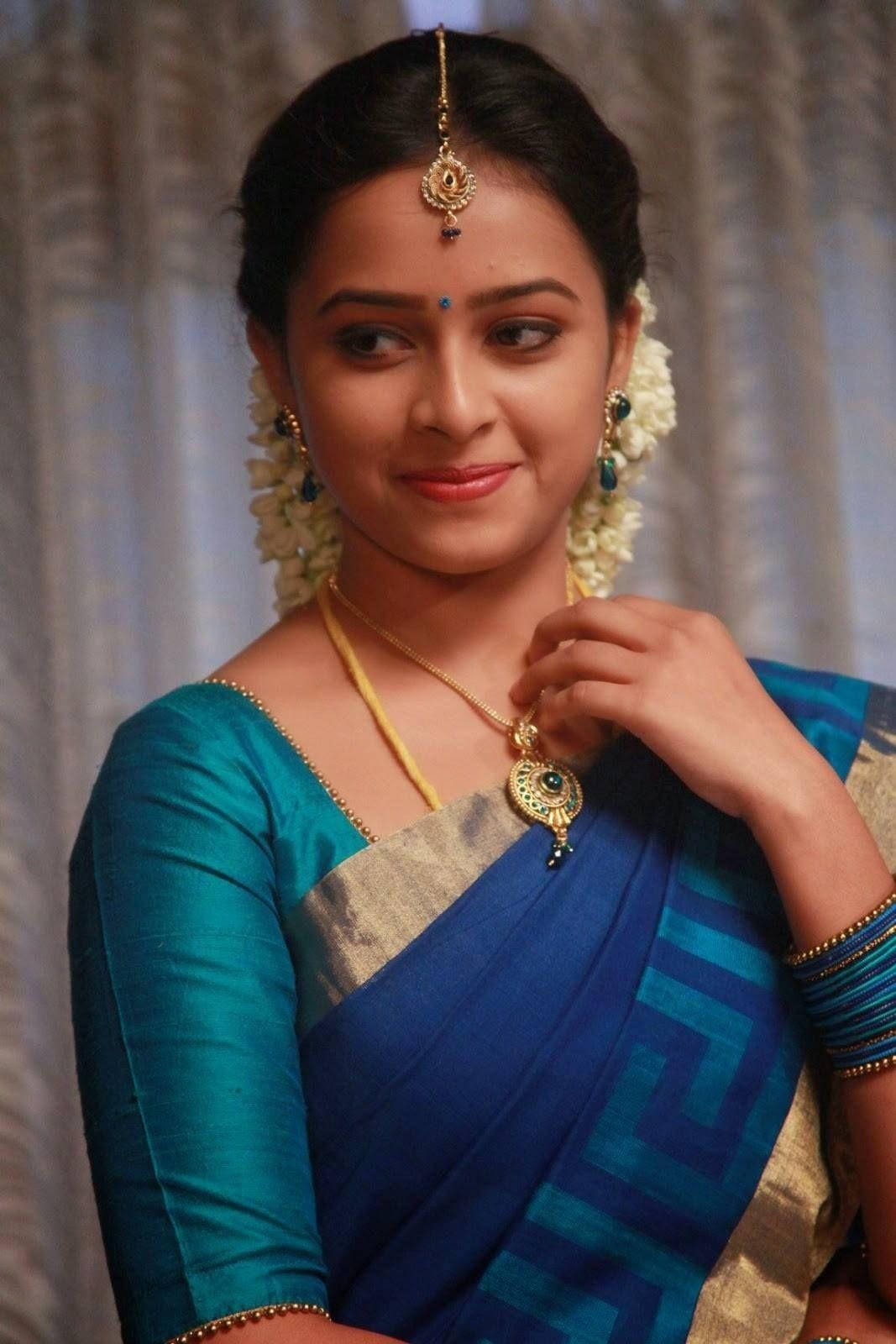 Tamil Actors HD 桌布 壁紙 — 一位身穿藍色和藍綠色紗麗、佩戴金色珠寶和白色花環的女性對著鏡頭溫柔微笑。
