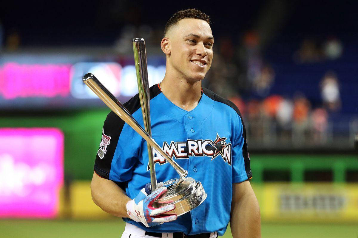 Stanton 桌布 壁紙 — 一位身穿藍色球衣、面帶微笑的棒球運動員在夜間燈光明亮的球場上，手持兩支球棒和一個獎盃。