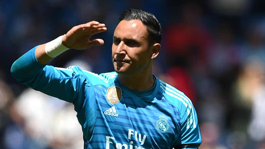 Keylor Navas 桌布 壁紙 — 一位身穿藍色皇家馬德里球衣的足球守門員在明亮的球場燈光下向球迷揮手。