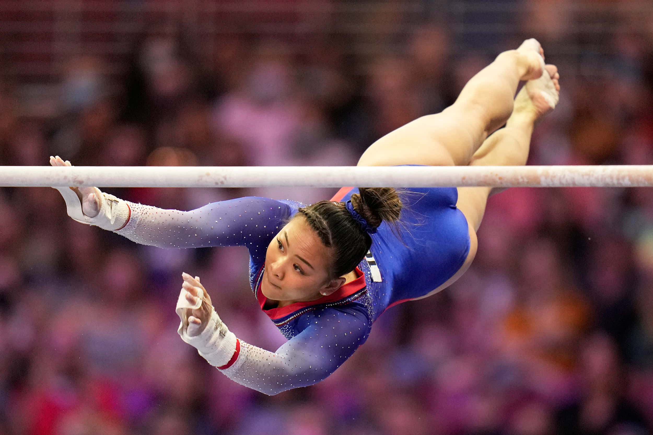 Olympics 桌布 壁紙 — 一位身穿藍色緊身衣的女子體操運動員在比賽中，以高度專注在單槓上完成一個動態翻轉。