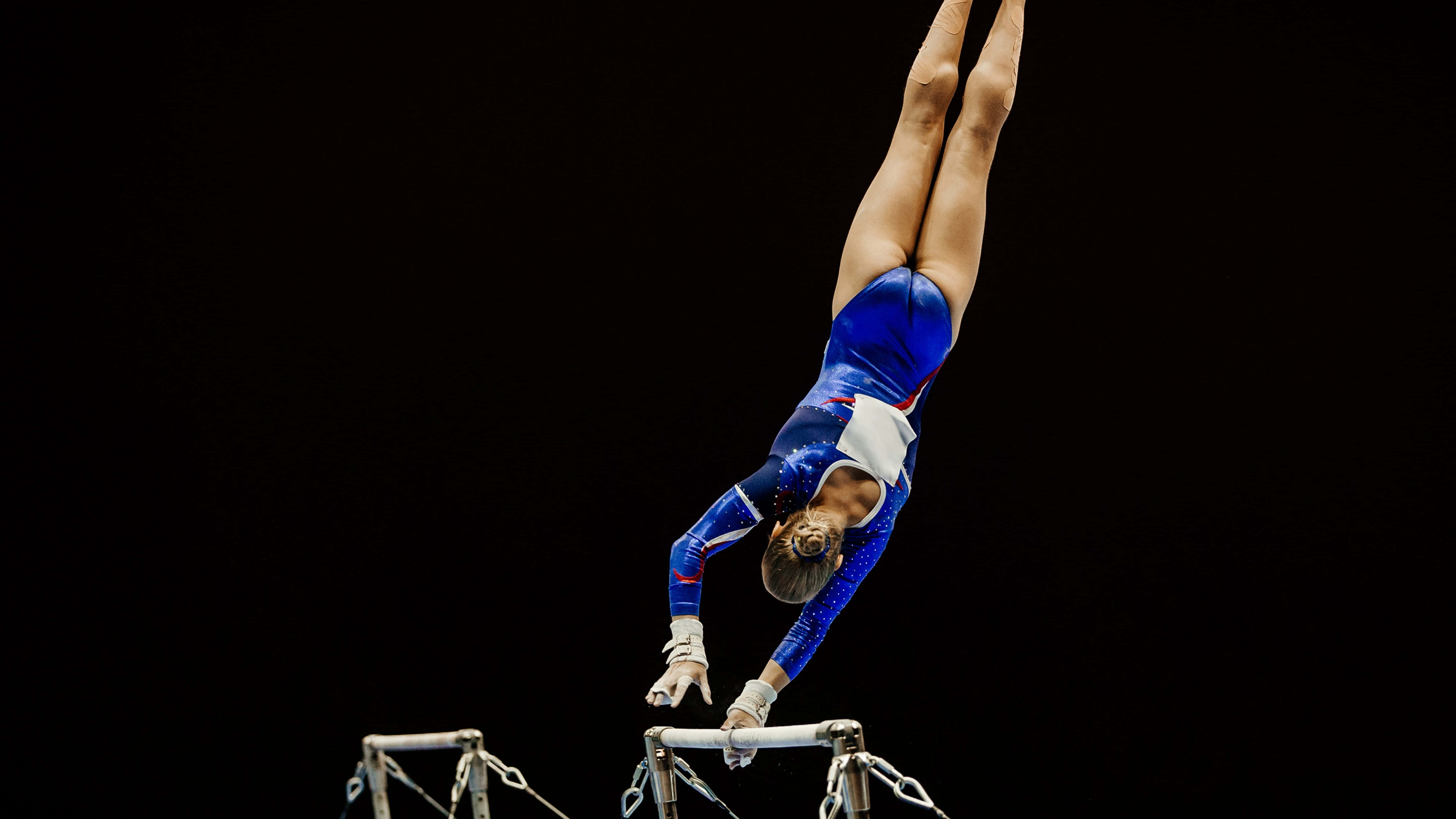 Gymnastics 桌布 壁紙 — 一位身穿藍色緊身連衣體操服的女體操運動員在黑色背景襯托下於雙槓上表演倒立。