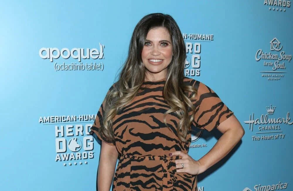 Danielle Fishel 桌布 壁紙 — 一位身穿虎紋連衣裙的女性在American Humane Hero Dog Awards的藍色背景前自信地微笑。