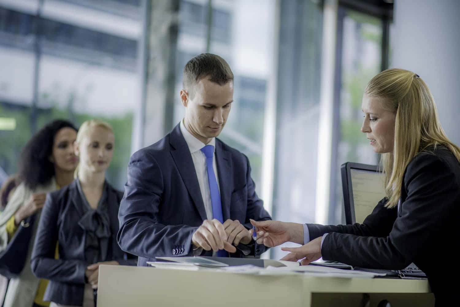 Bank 桌布 壁紙 — 一位身穿西裝的商人在現代辦公桌前與接待員互動時查看手錶。