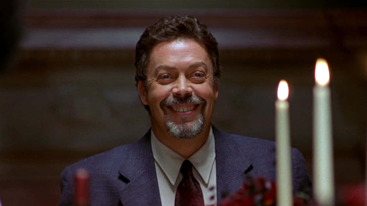 Tim Curry 桌布 壁紙 — 一位身穿西裝的微笑男士在昏暗的房間裡，在閃爍的蠟燭旁散發溫暖的光芒。