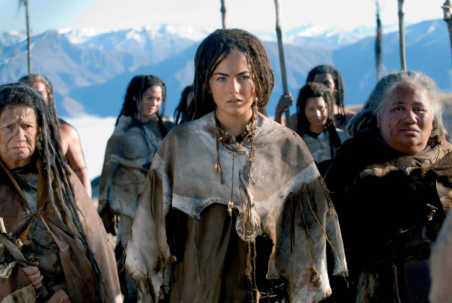 Camilla Belle 桌布 壁紙 — 一位身穿部落服飾的堅定女性，與一群戰士站在畫面中央，背景是白雪覆蓋的山脈。