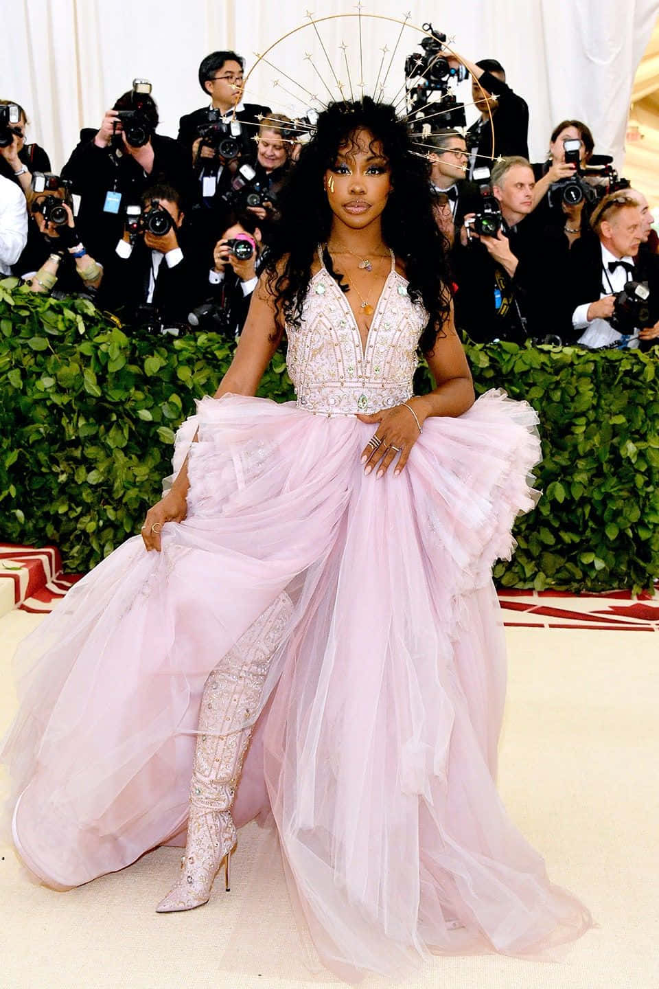 Met Gala 桌布 壁紙 — 一位身穿閃亮粉紅色長裙及相配大腿靴的女性，在攝影師包圍的紅地毯上自信地擺姿勢。