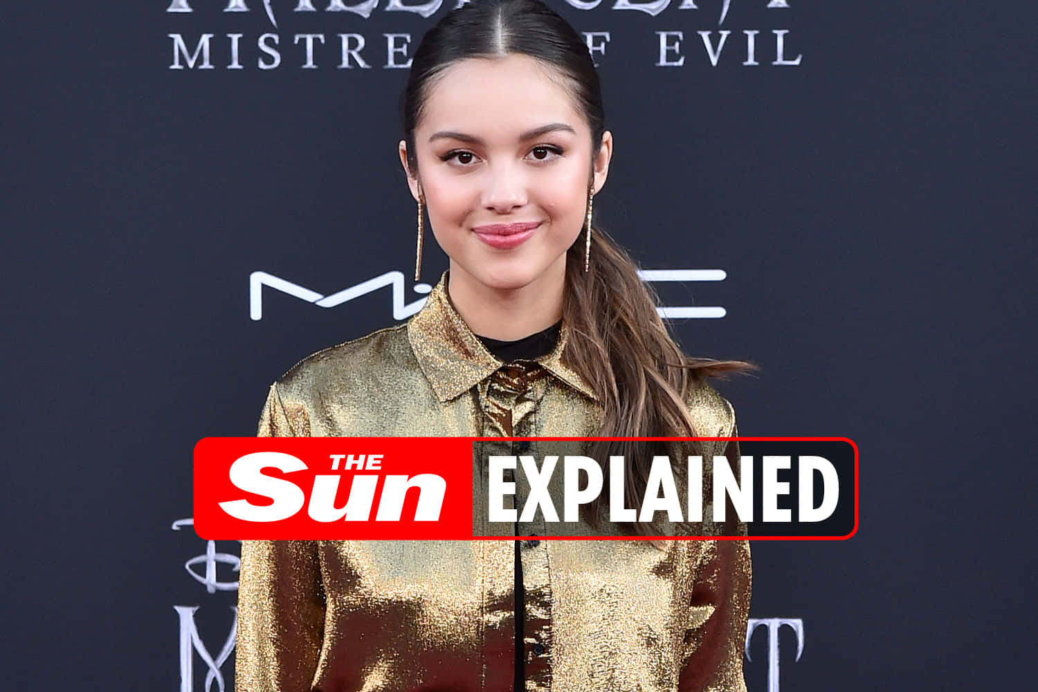 Olivia Rodrigo 桌布 壁紙 — 一位身穿閃亮金色外套的女性在深色背景及活動標誌前對著鏡頭微笑。