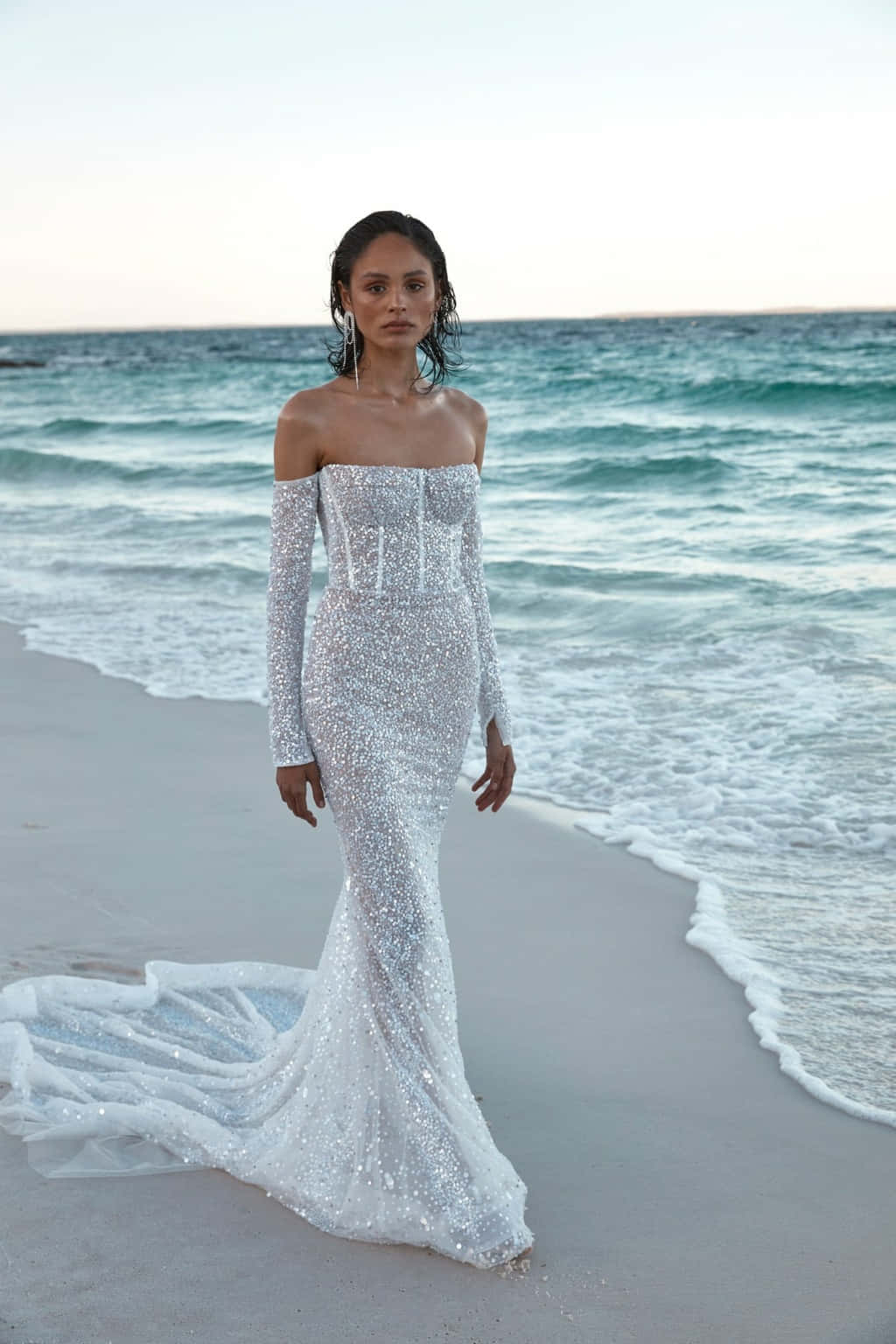 Bride's Dress 桌布 壁紙 — 一位身穿閃亮銀色美人魚婚紗的女性站在沙灘上，身後海浪拍打。