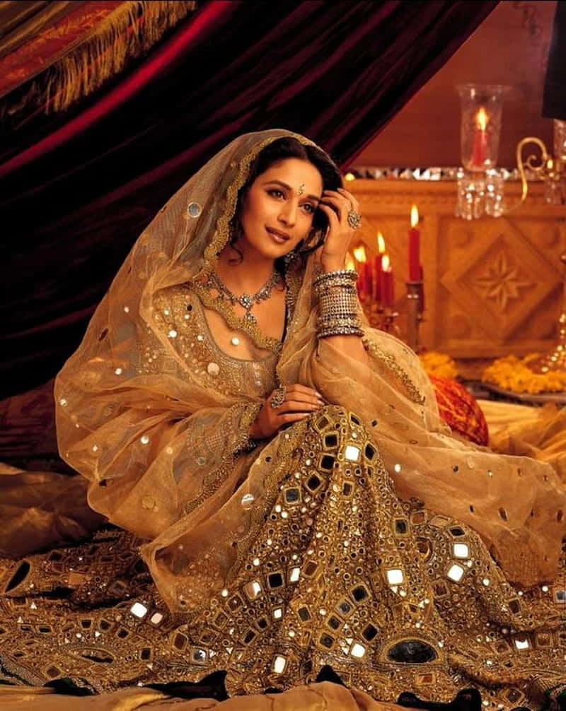  壁紙 — 一位身穿閃閃發光金色刺繡長裙（Lehenga）的女性，優雅地坐在紅色天鵝絨帷幔下，點燃的蠟燭散發出溫暖的光芒。