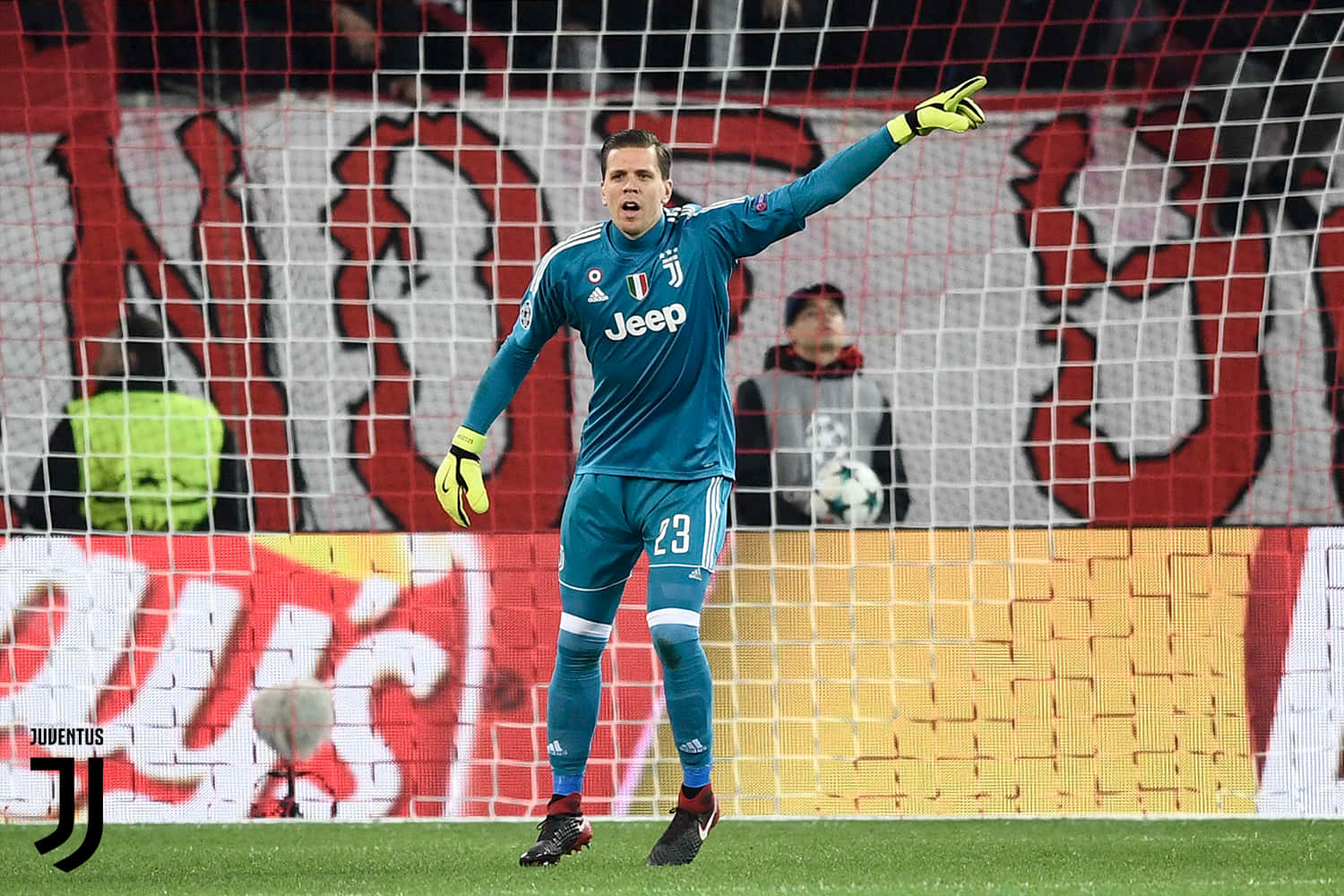 Wojciech Szczesny 桌布 壁紙 — 一位身穿青綠色球衣的祖雲達斯門將，在燈光璀璨的足球場上，身後有球迷和球門網，他正有力地做著手勢。