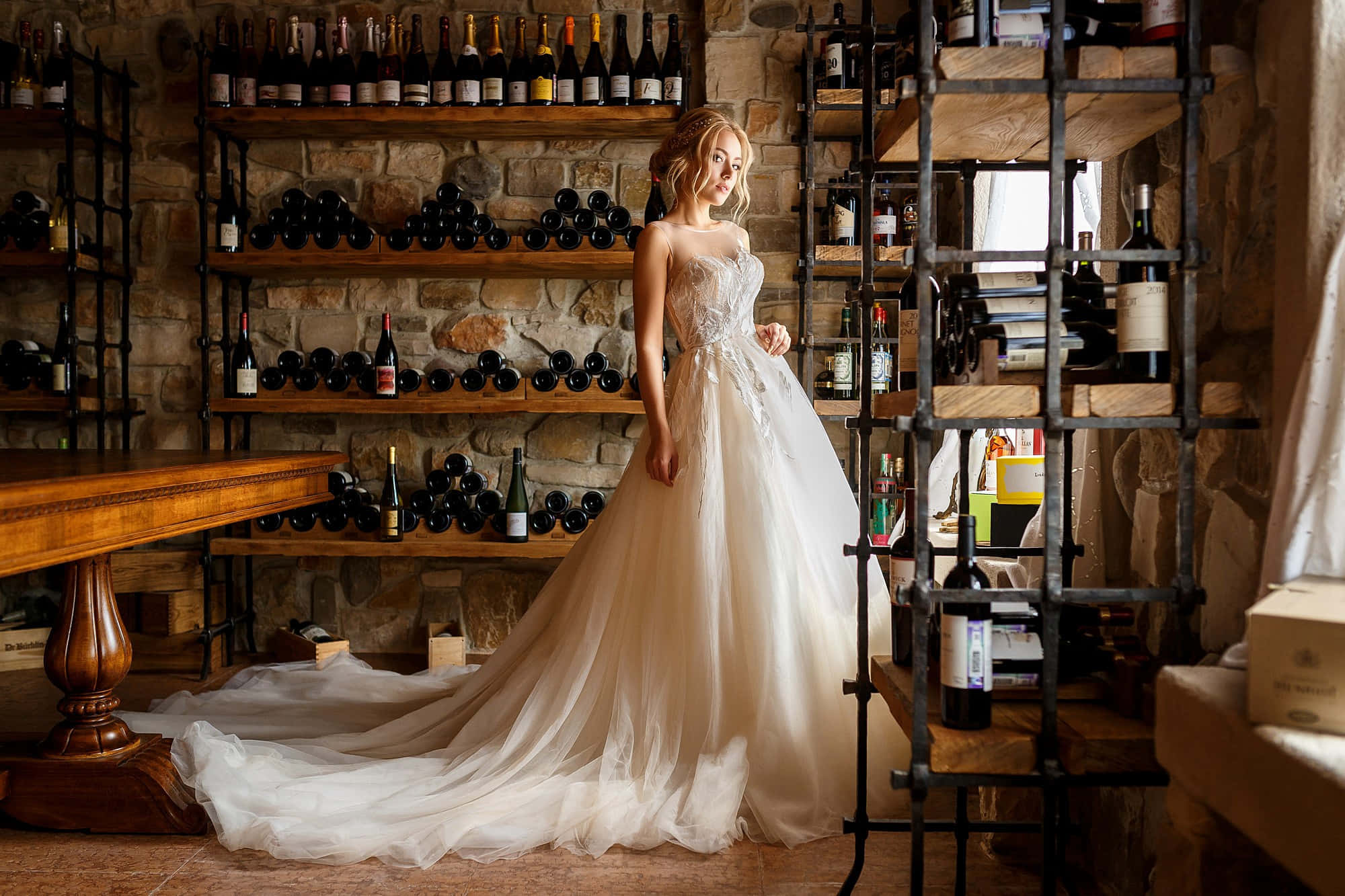 Wedding Dress 桌布 壁紙 — 一位身穿飄逸白色婚紗的新娘，優雅地站在一個質樸的石砌酒窖中，酒窖內有木架擺滿酒瓶。