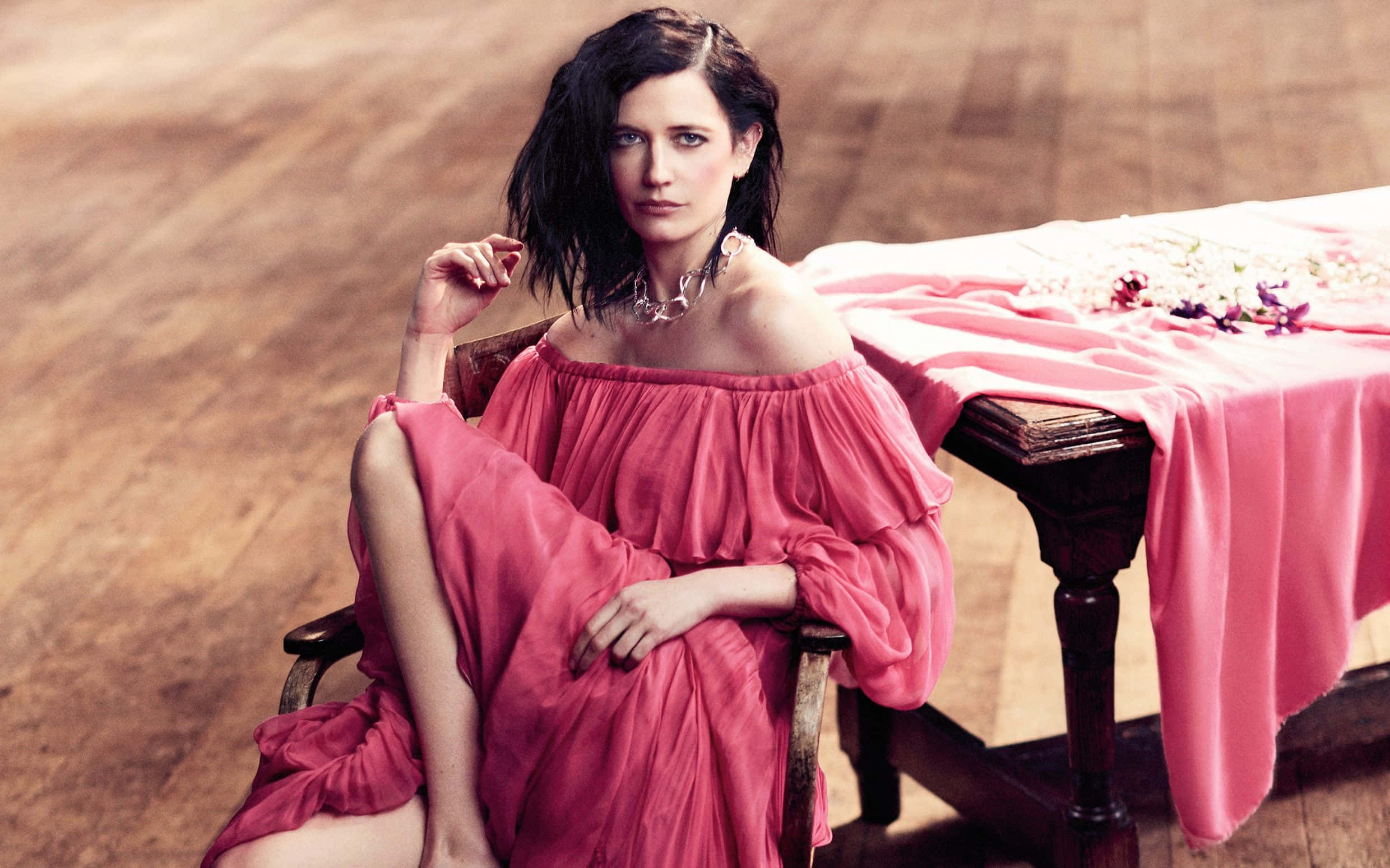 eva green 桌布 壁紙 — 一位身穿飄逸粉紅色露肩連衣裙的女性優雅地坐在木椅上，旁邊是鋪著桌布並擺滿鮮花的桌子。