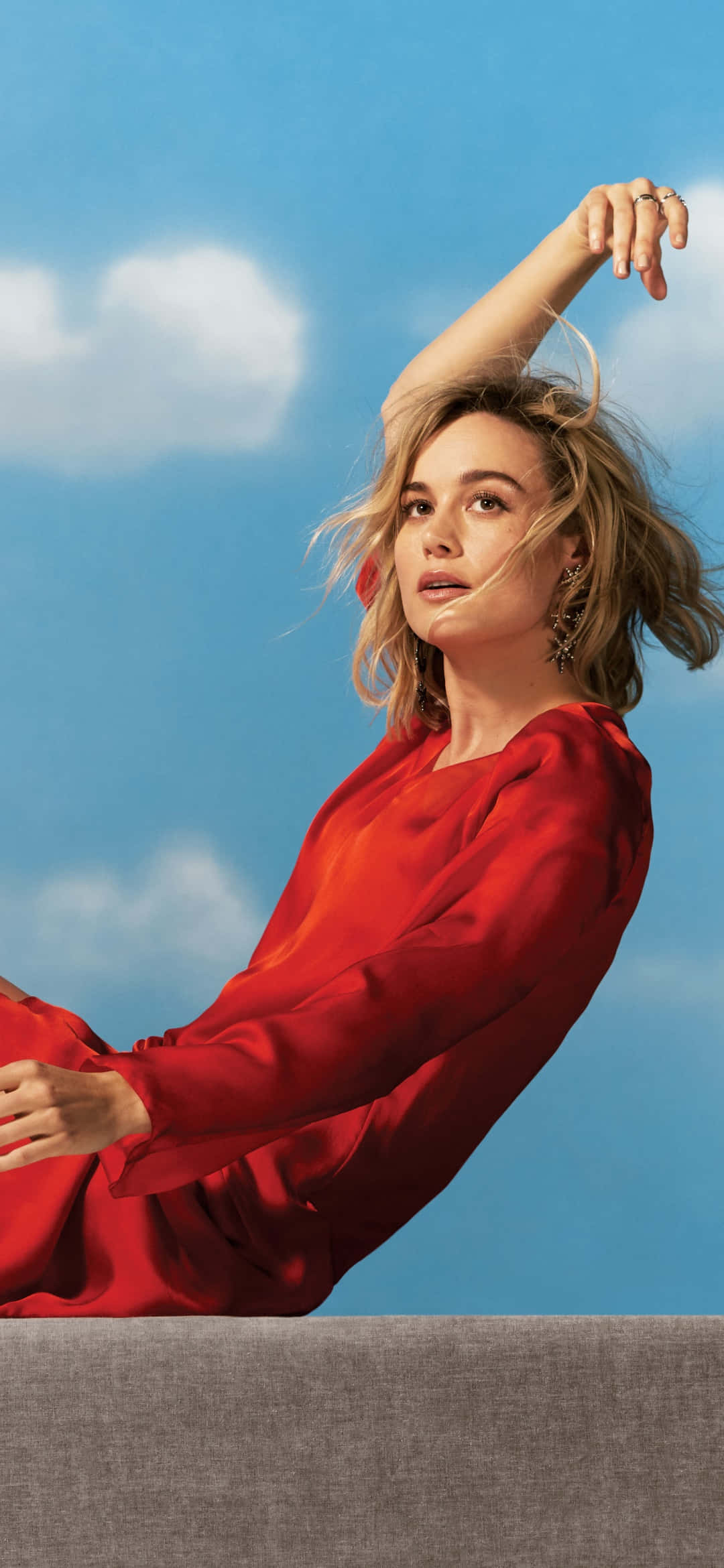 brie larson 桌布 壁紙 — 一位身穿飄逸紅裙的女性在藍天白雲下優雅地擺姿勢。