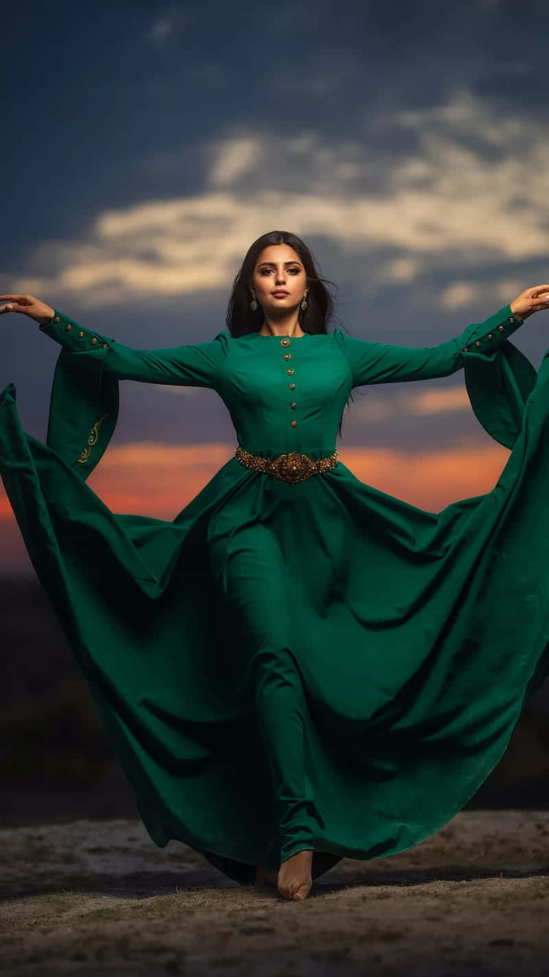 Green Fashion 桌布 壁紙 — 一位身穿飄逸翡翠綠長裙的女性，在橙紫相間雲彩的戲劇性日落天空下優雅地旋轉。