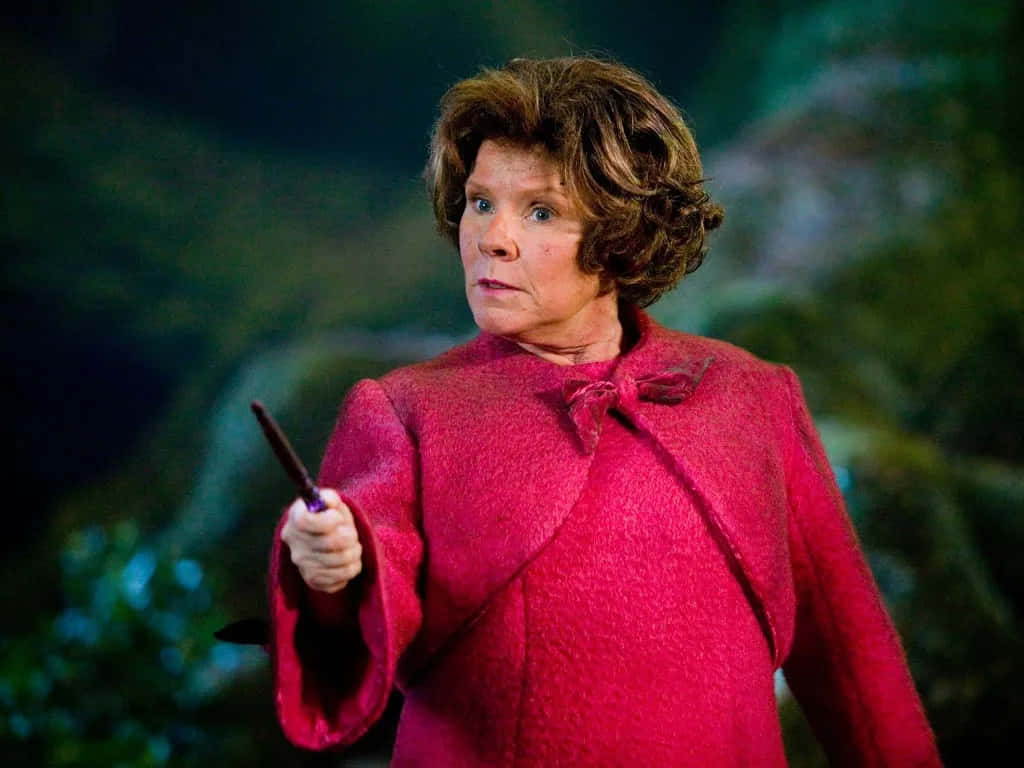 The Hogwarts Professors 桌布 壁紙 — 一位身穿鮮紅色外套的女性，在模糊的綠色森林背景下，手持魔杖，神情專注。