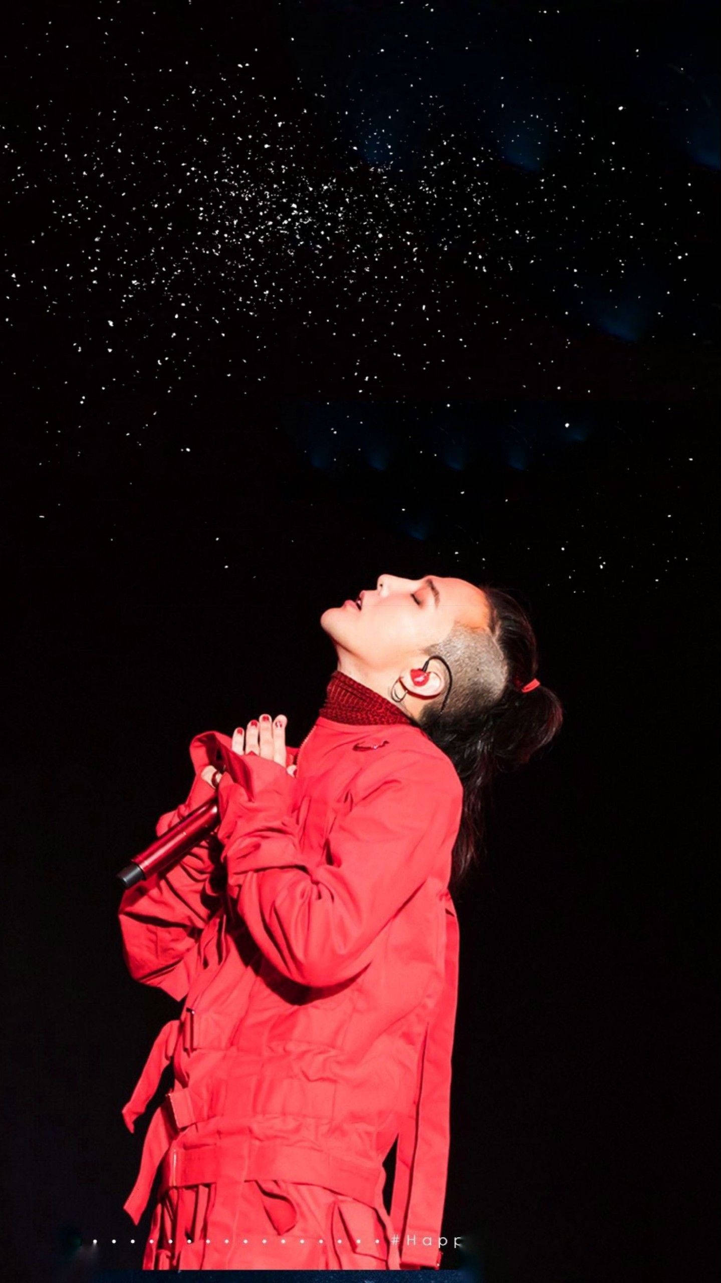 G-DRAGON Act III 壁紙 — 一位身穿鮮紅色服裝的表演者雙手合十仰望，閃爍的粒子在黑暗的星空背景下飄落。