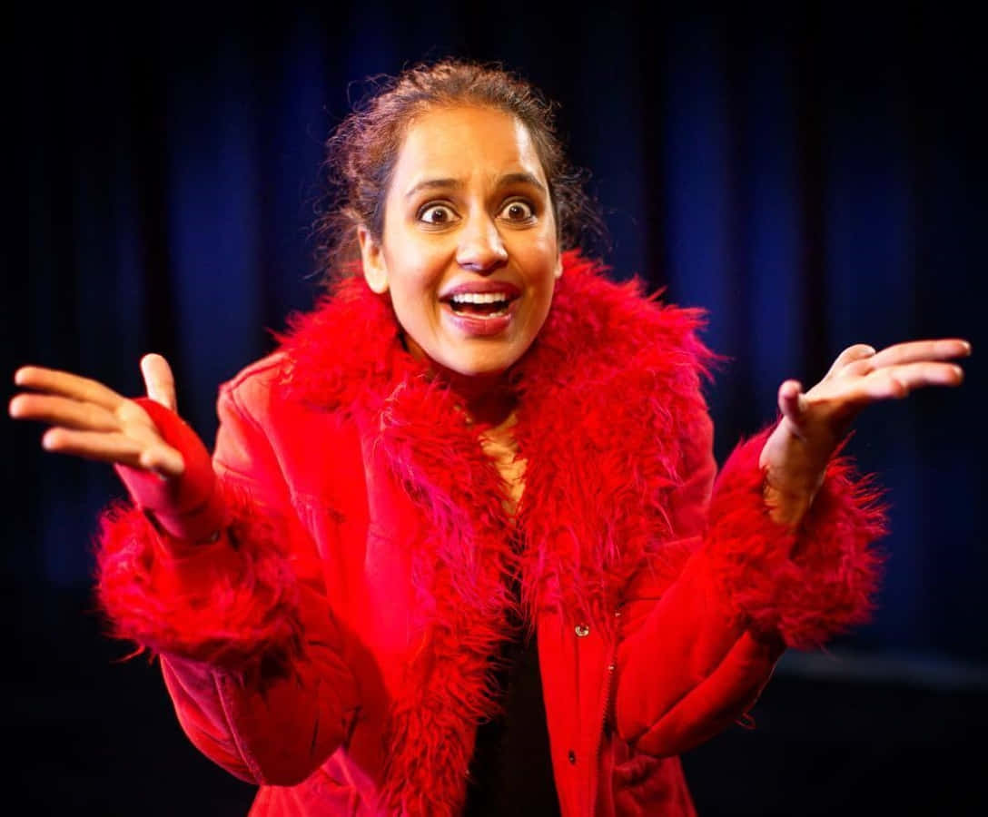 Agam Darshi 桌布 壁紙 — 一位身穿鮮紅色羽毛外套的女性，在深藍色窗簾背景下擺出驚訝的姿勢。