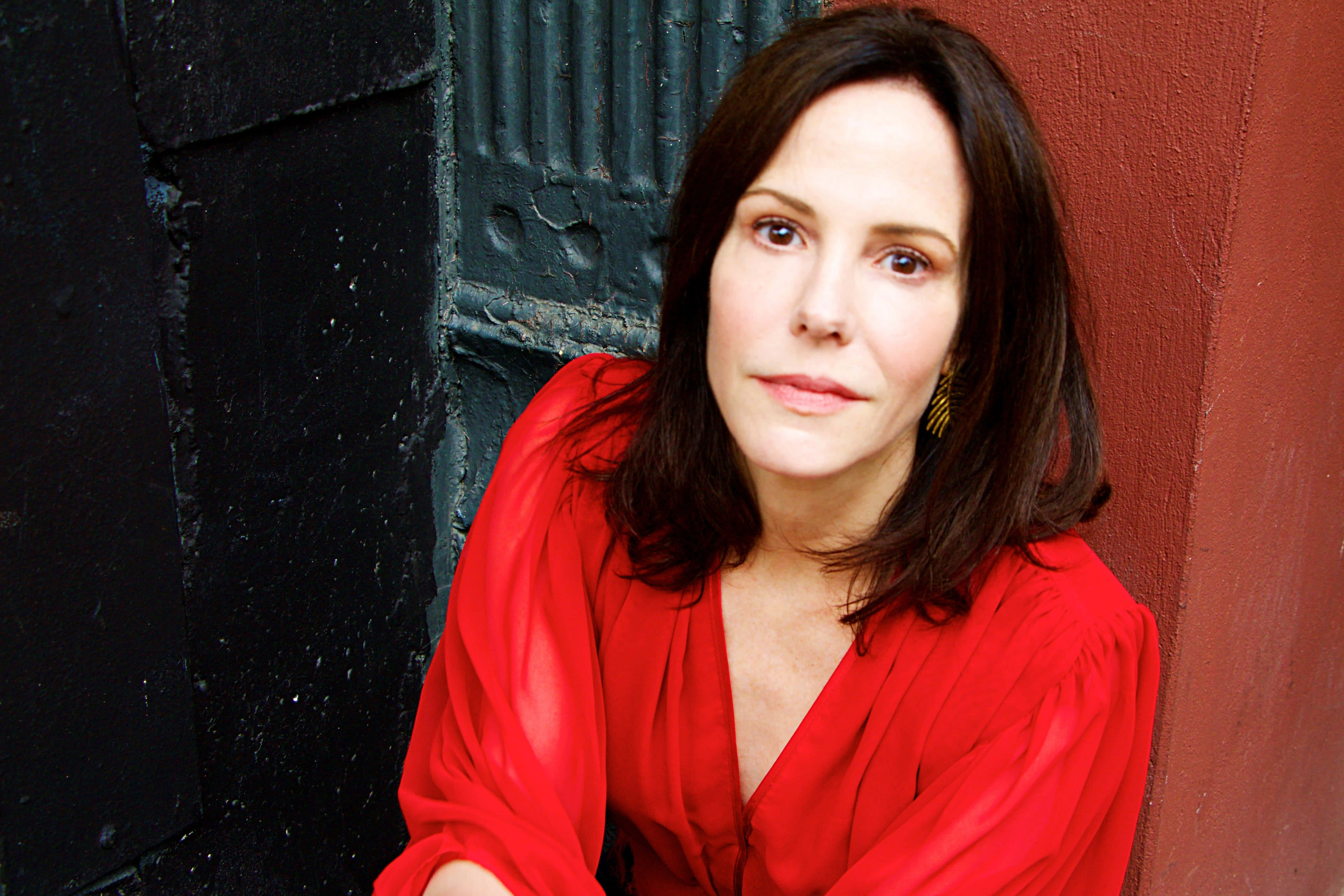 mary louise parker 桌布 壁紙 — 一位身穿鮮紅色襯衫的女性靠在一面對比強烈的黑紅牆上，目光平靜而直接。