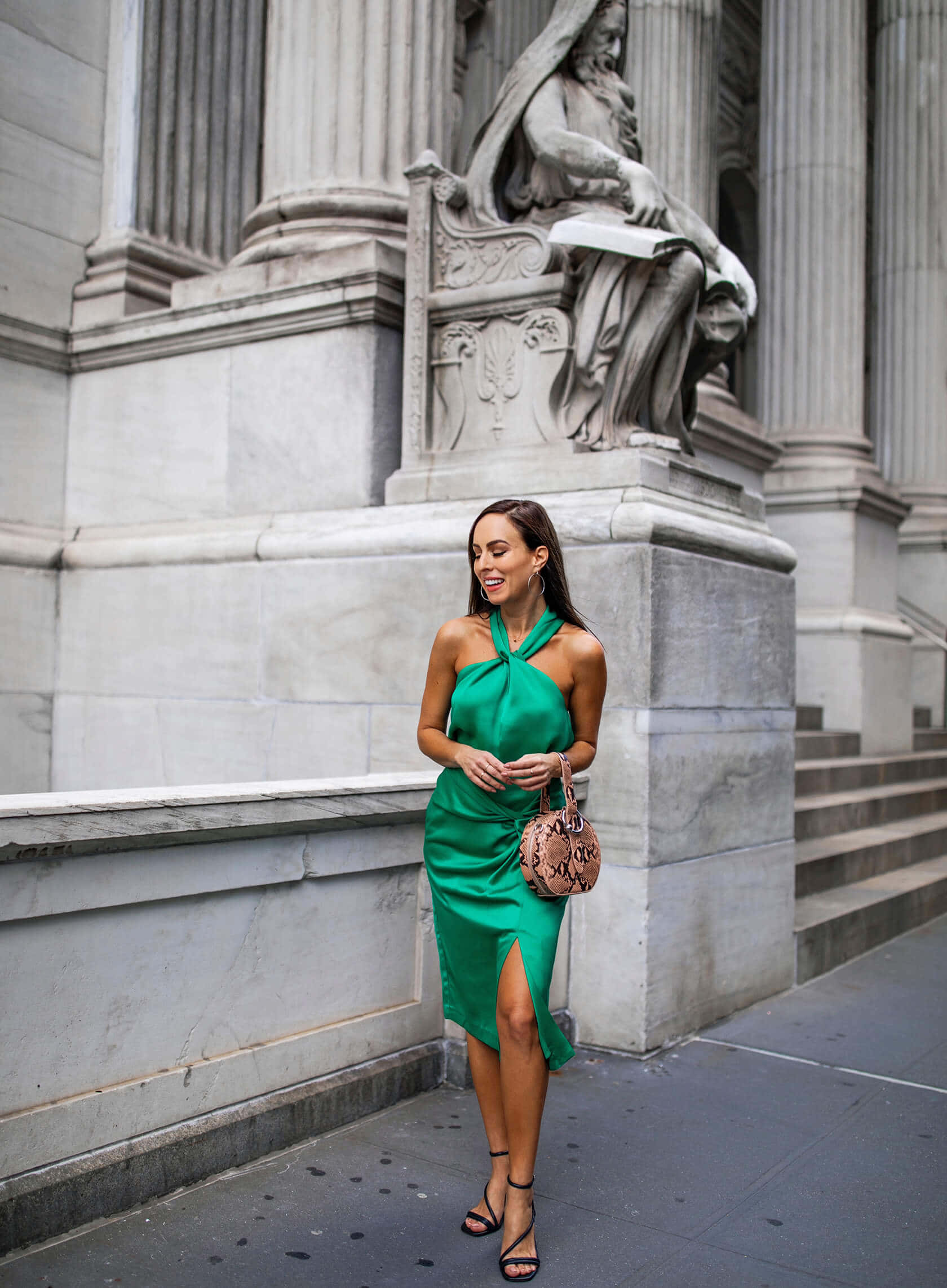 Green Fashion 桌布 壁紙 — 一位身穿鮮綠色緞面連衣裙的女性在經典的城市環境中，站在一座宏偉的大理石雕像旁微笑。