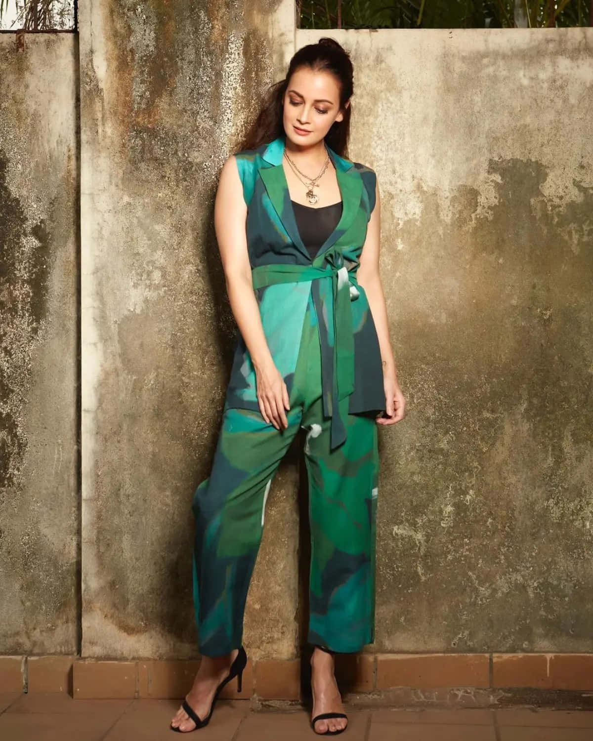 Green Fashion 桌布 壁紙 — 一位身穿鮮豔綠色圖案連身褲的女性，神情平靜地靠在一面風化的混凝土牆上。