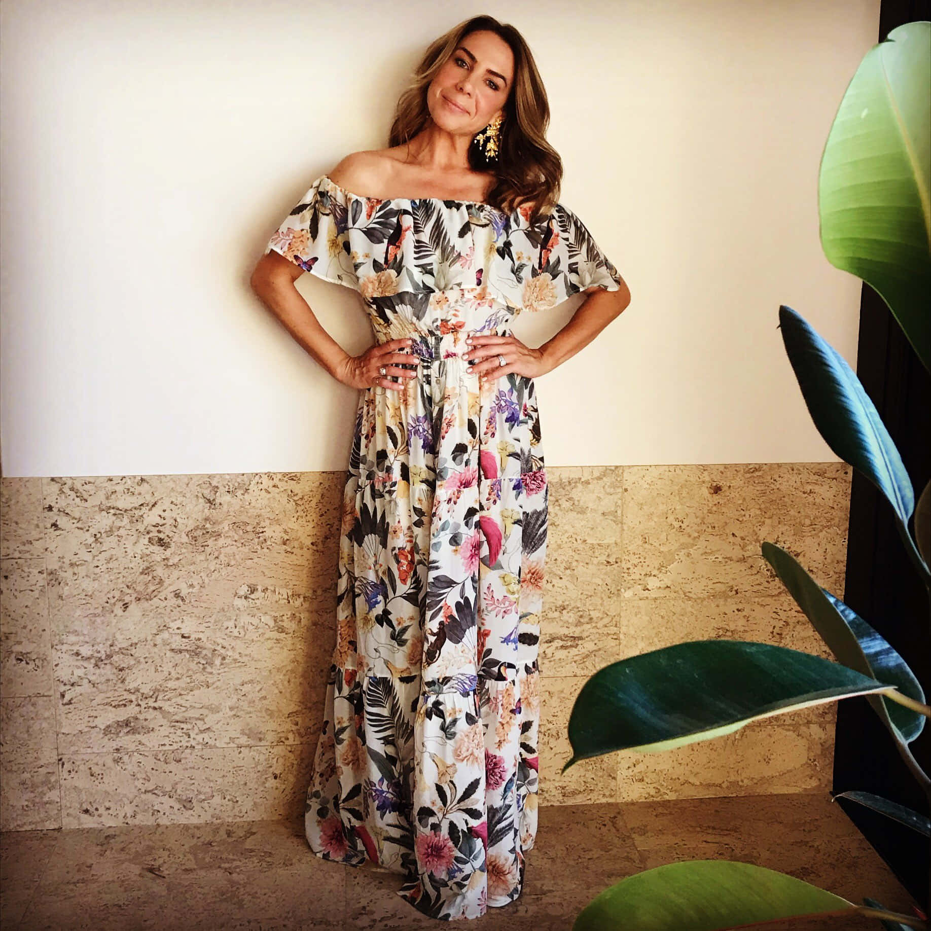Kate Ritchie 桌布 壁紙 — 一位身穿鮮豔花卉露肩長裙的女性，在雙色牆前與茂盛綠色植物旁自信地擺姿勢。