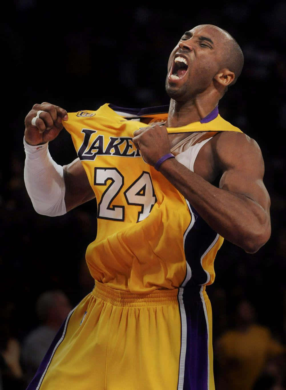 科比· Bryant 桌布 壁紙 — 一位身穿黃色湖人隊24號球衣的籃球運動員在昏暗的場館中撕破球衣，勝利地吶喊。