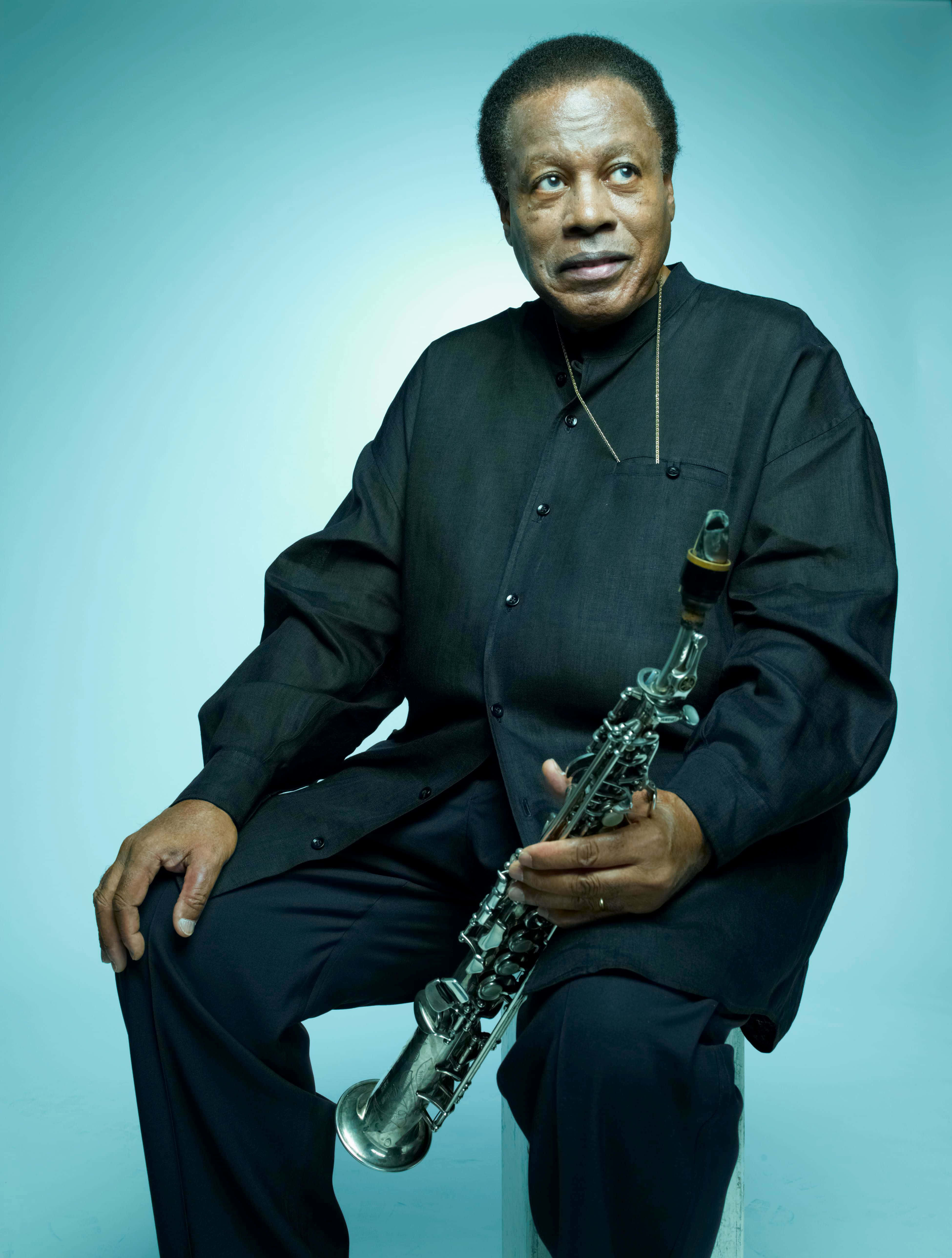 Wayne Shorter 桌布 壁紙 — 一位身穿黑色服裝的優雅爵士薩克斯風手，在柔和的藍色攝影棚背景下手持樂器。
