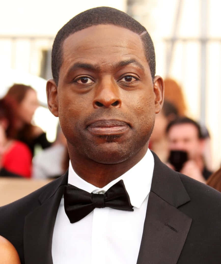 Sterling K Brown 桌布 壁紙 — 一位身穿黑色燕尾服和領結的男士在正式活動中的特寫肖像，背景人物模糊。
