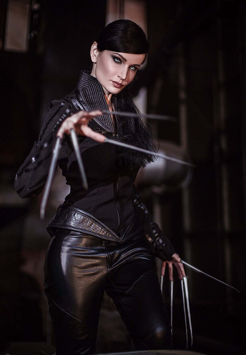 Lady Deathstrike 桌布 壁紙 — 一位身穿黑色皮革的兇猛女性在昏暗的工業環境中揮舞金屬爪。