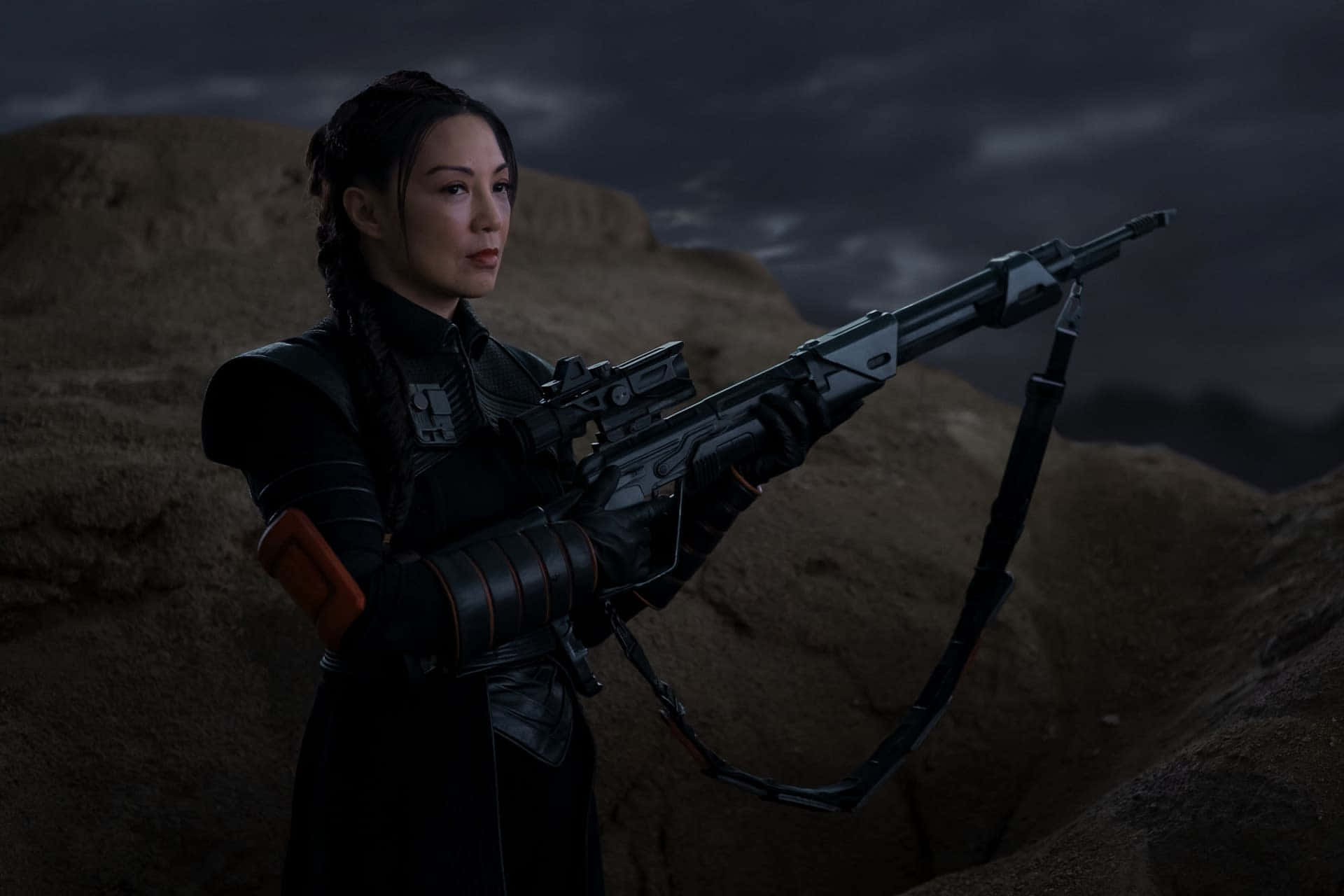 Ming Na Wen 桌布 壁紙 — 一位身穿黑色盔甲的女戰士，在黑暗暴風雨的沙漠背景下手持重型爆能步槍。