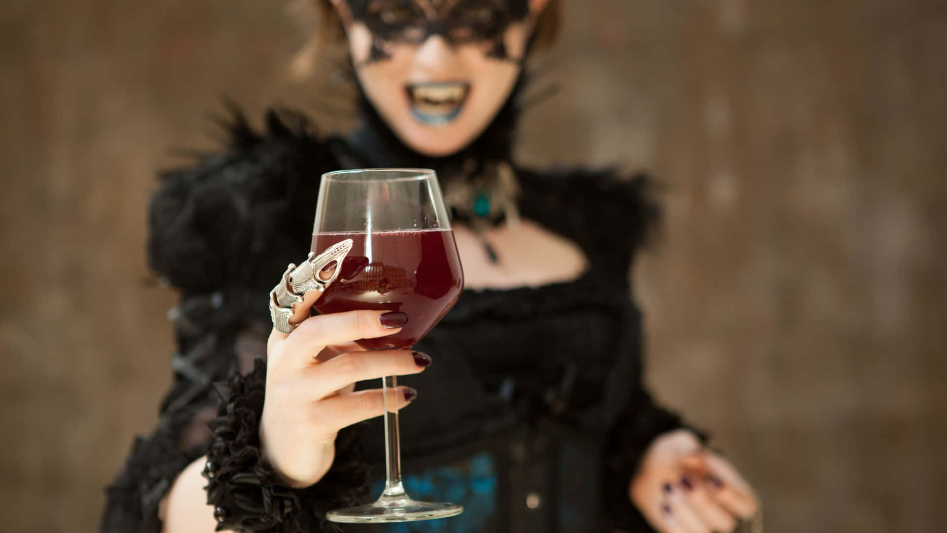 Goth 桌布 壁紙 — 一位身穿黑色羽毛服裝、戴著面具的女性，帶著戲劇性的笑容手持一杯紅酒。