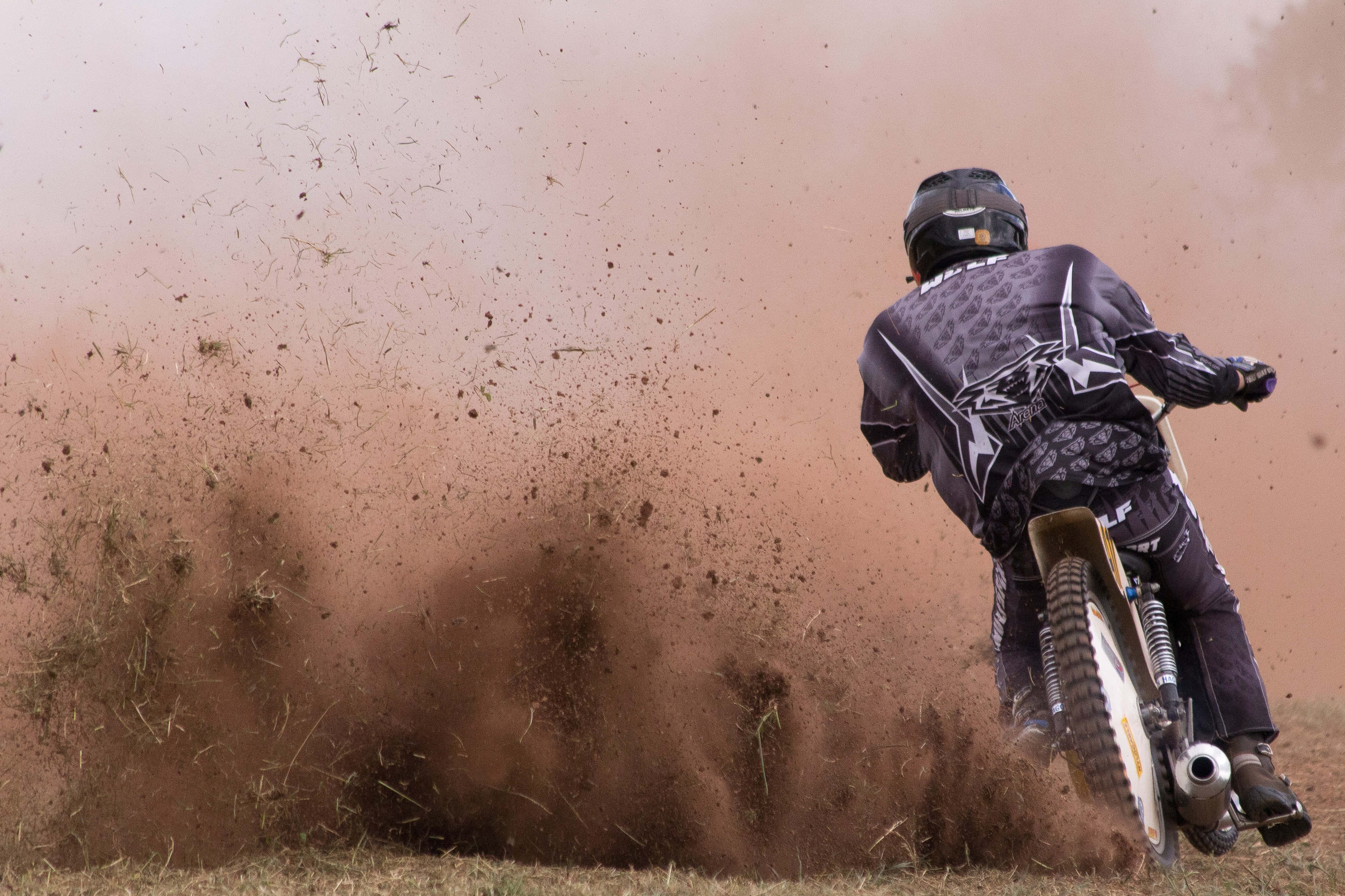 Dust 桌布 壁紙 — 一位身穿黑色裝備的越野電單車手在草地上飛馳，揚起大片棕色塵土。