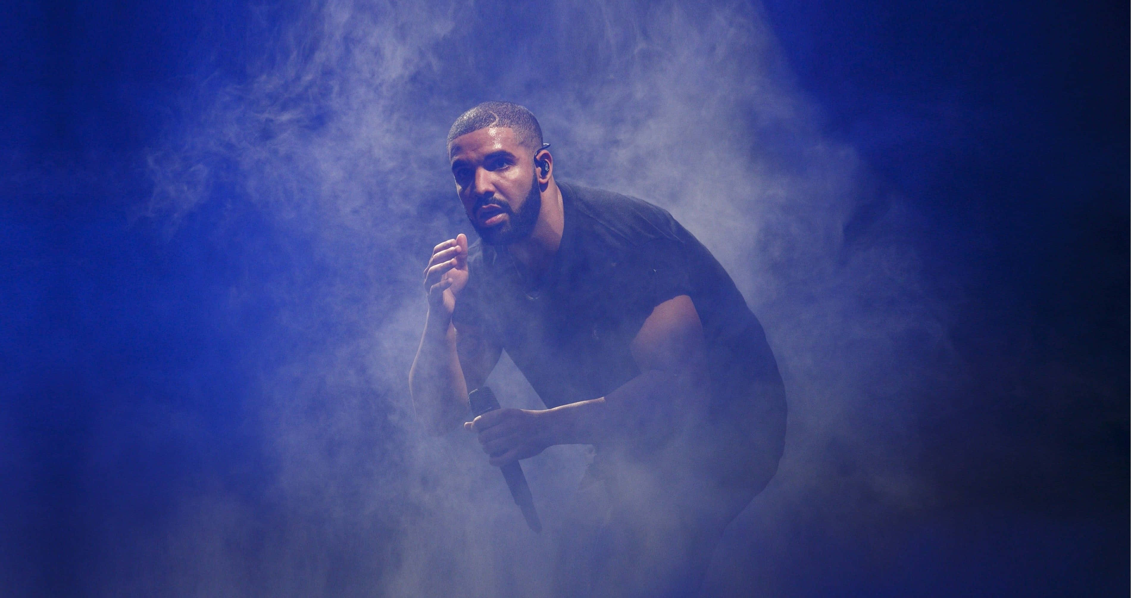 Drake 桌布 壁紙 — 一位身穿黑色襯衫的男性表演者在戲劇性的舞台燈光下，於旋轉的藍色煙霧中手持麥克風。