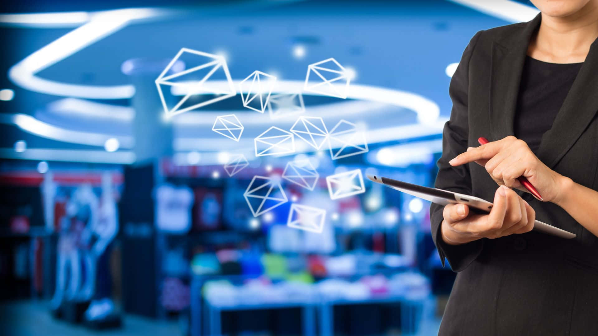 Email 桌布 壁紙 — 一位身穿黑色西裝的女商人在現代零售店中與平板電腦上方漂浮的發光電子郵件圖標互動。