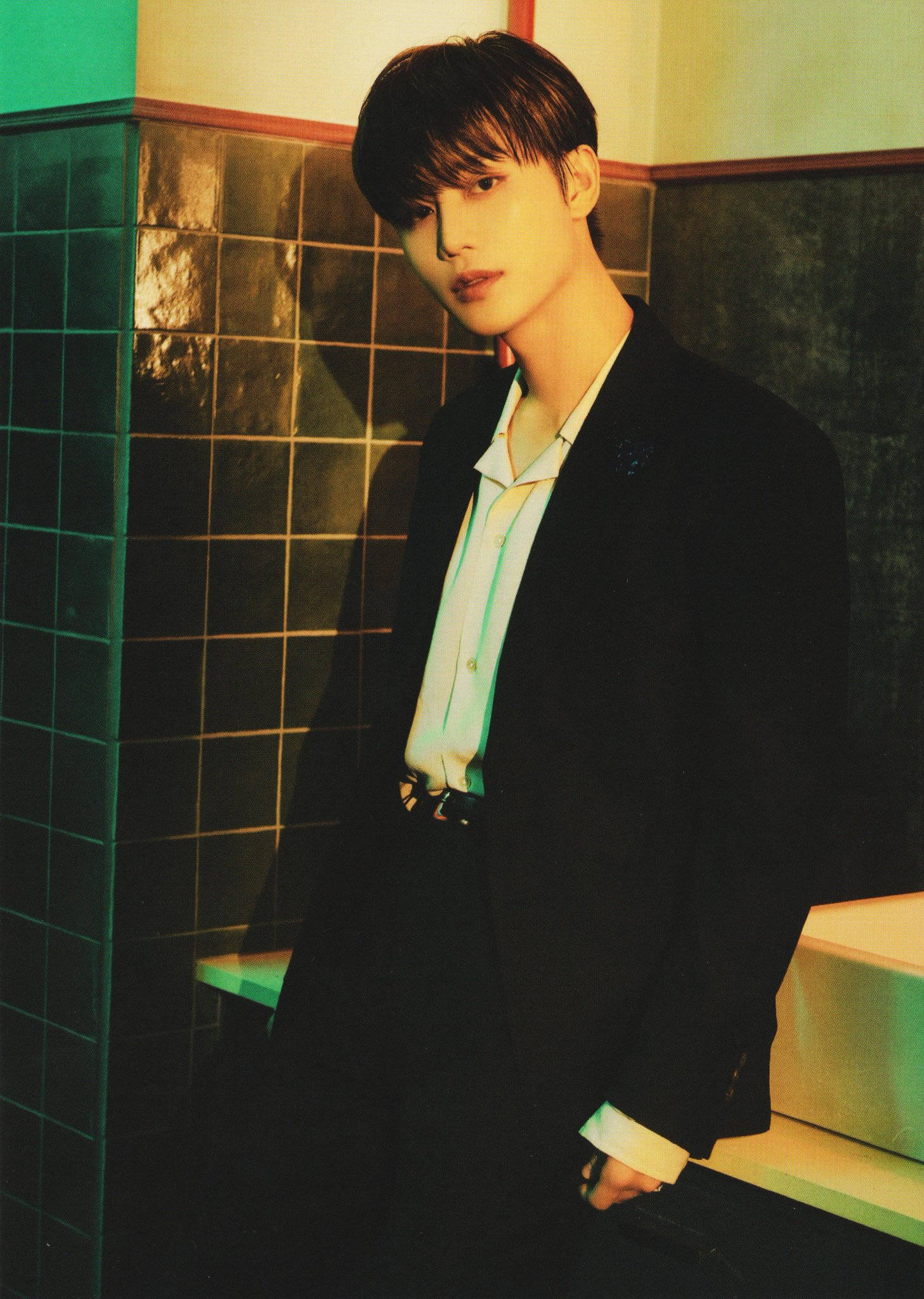 NCT 127 Taeil Favorite 壁紙 — 一位身穿黑色西裝的年輕男子，在溫暖的電影燈光下，站在綠色瓷磚牆前。