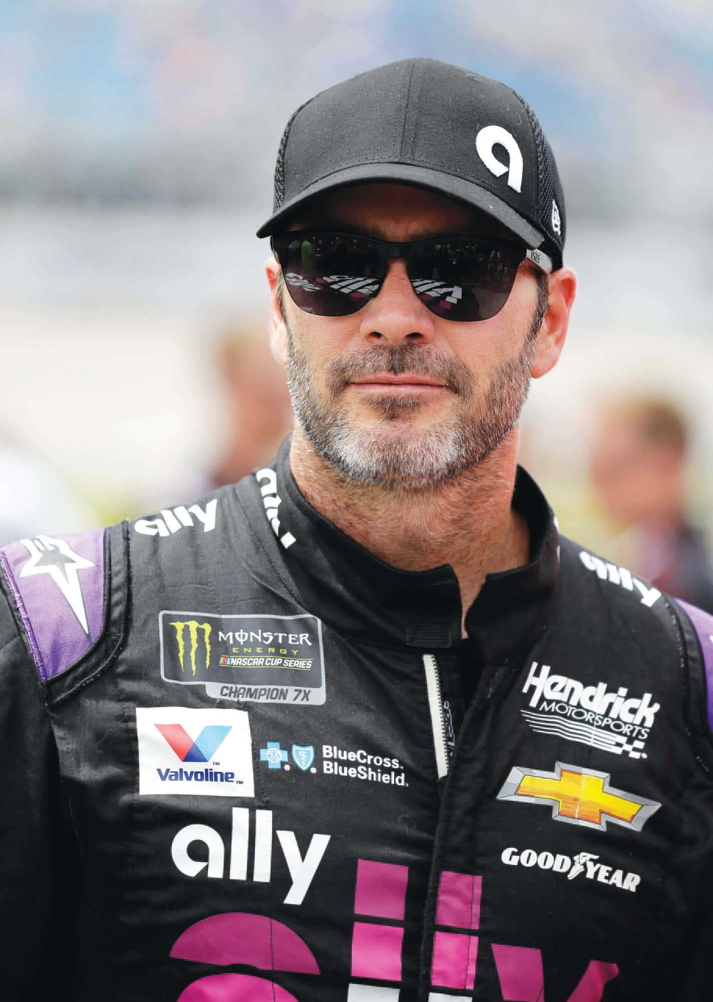 Jimmie Johnson 桌布 壁紙 — 一位身穿黑色賽車服和帽子的NASCAR車手，戴著太陽眼鏡，鏡片反射出賽道燈光，凝視前方。