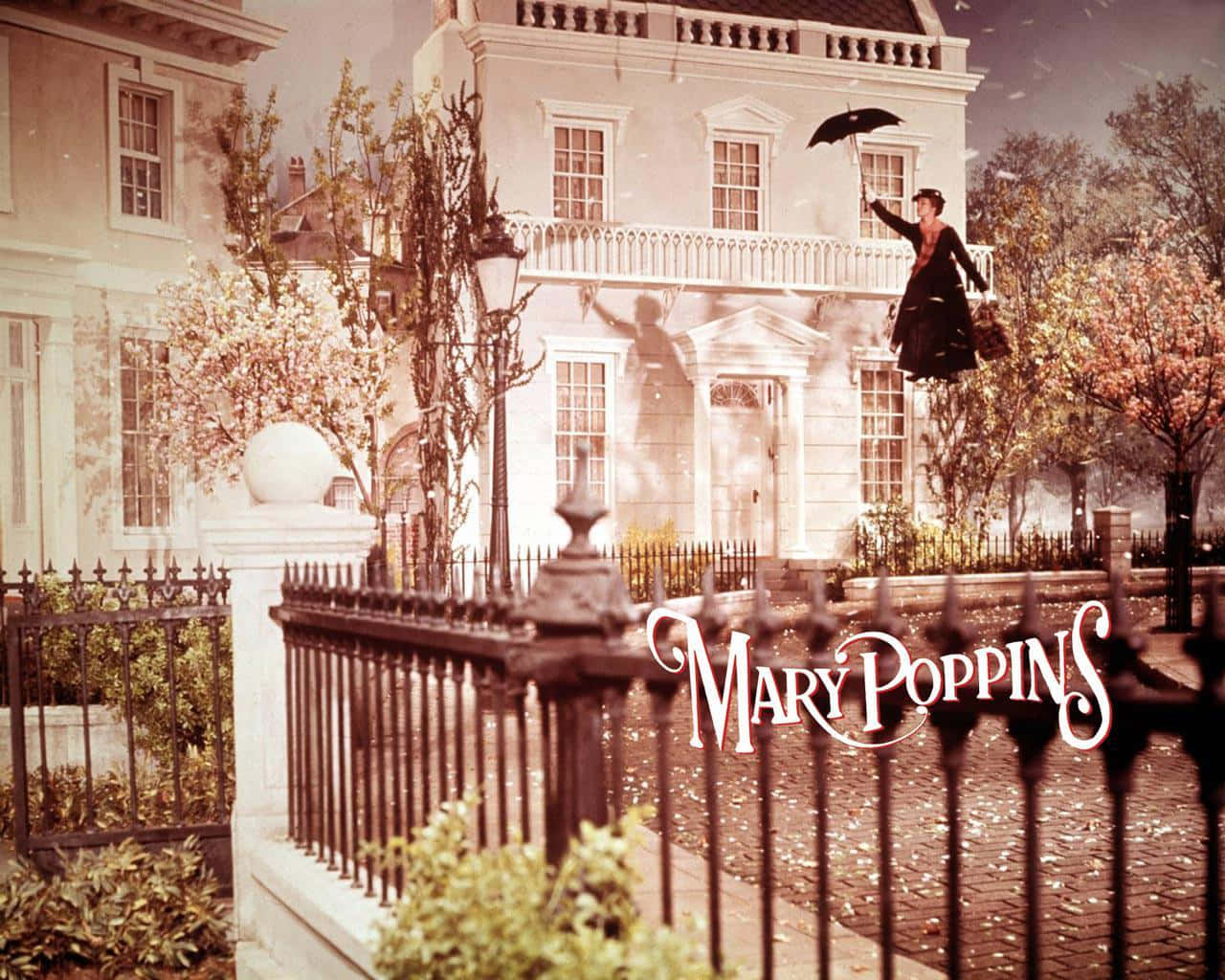 mary poppins 桌布 壁紙 — 一位身穿黑色連衣裙的女子飄浮在維多利亞式房屋上方，手持雨傘，樹葉在空中飄動。