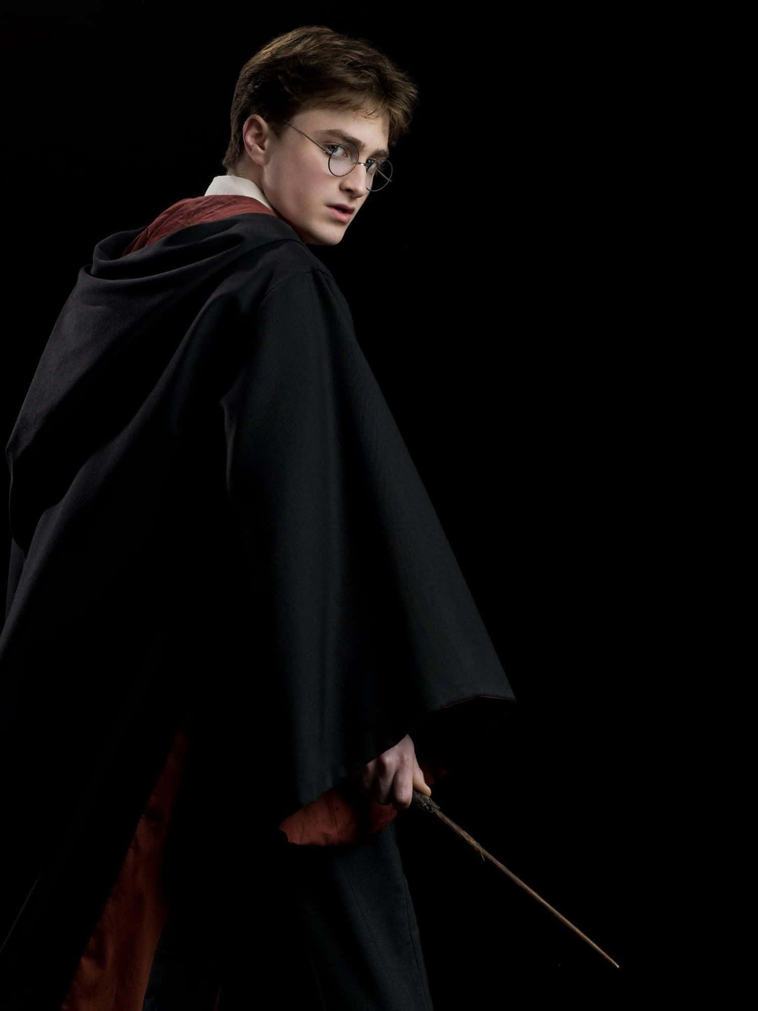 The Half-blood Prince 桌布 壁紙 — 一位身穿黑色長袍、戴眼鏡的年輕巫師，手持魔杖，在純黑背景上回頭望向身後。