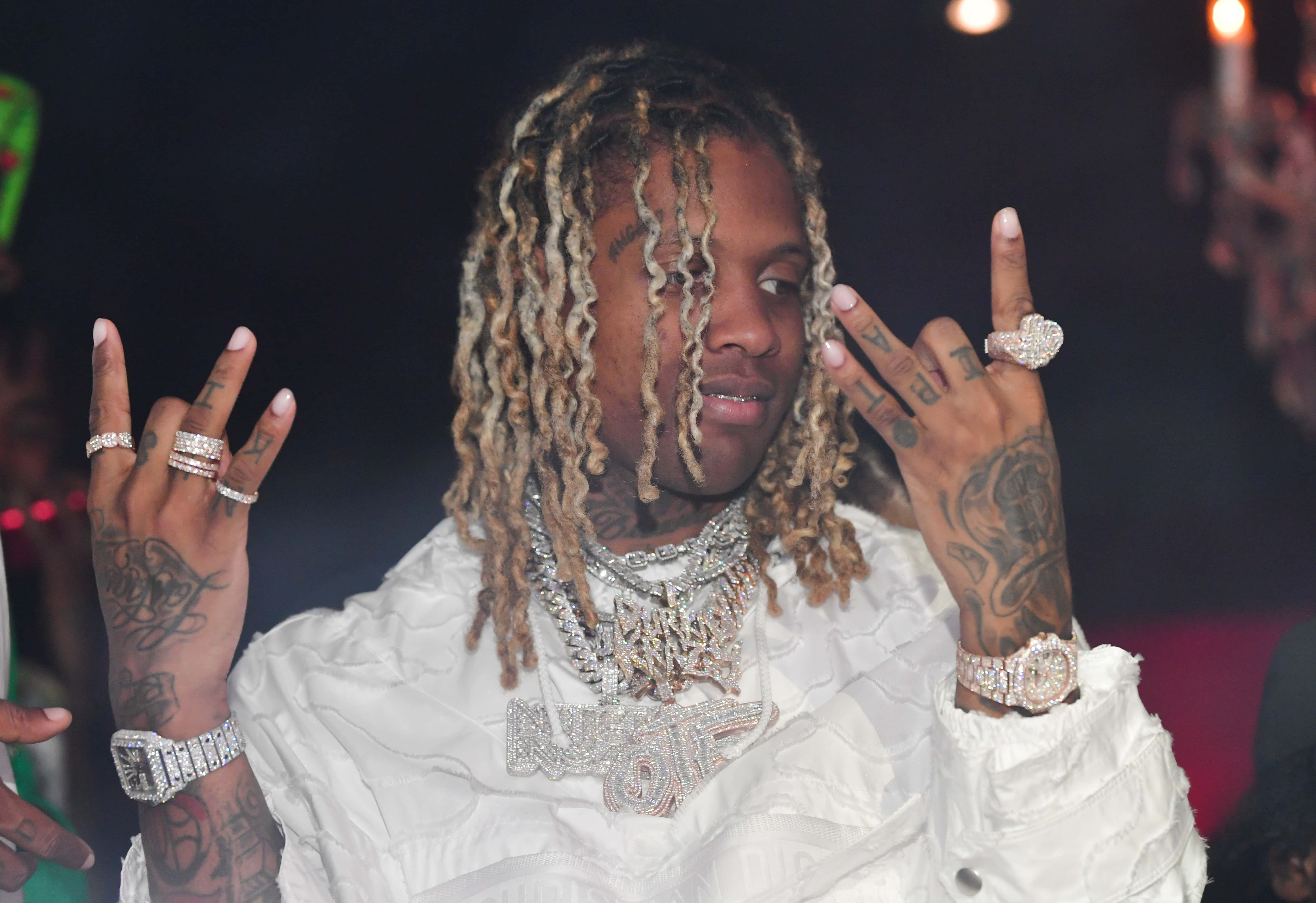 lil durk 桌布 壁紙 — 一位辮子頭和紋身的說唱歌手，在昏暗的俱樂部燈光下穿著白色服裝，閃耀著鑲鑽戒指和鏈條。