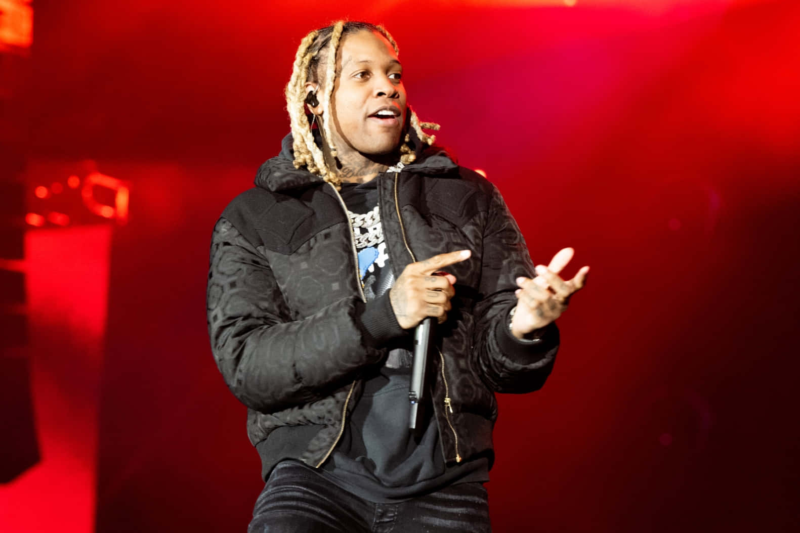 lil durk 桌布 壁紙 — 一位辮子頭說唱歌手在強烈紅光下手持麥克風，在舞台上充滿活力地表演。