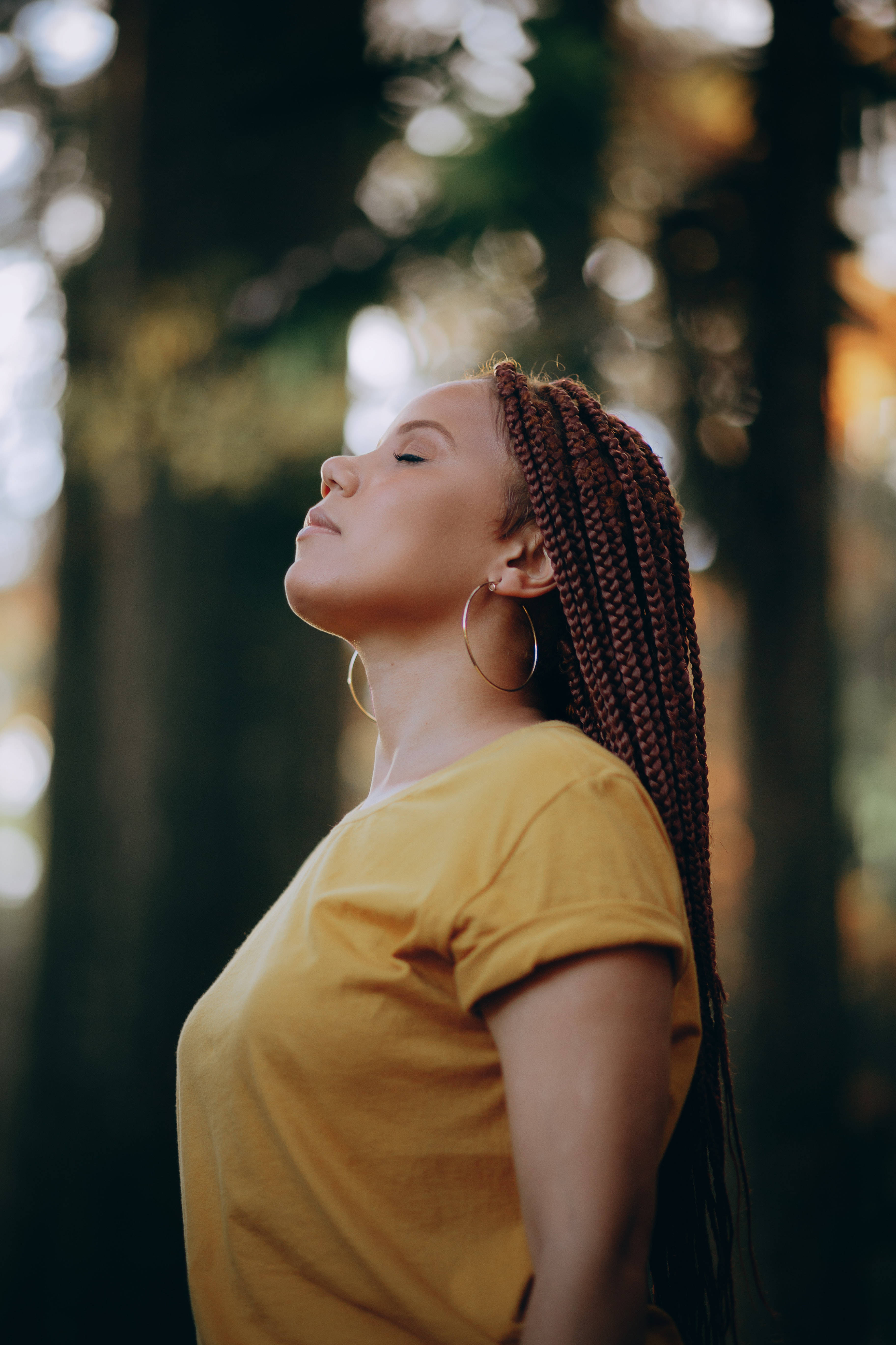 Meditation 桌布 壁紙 — 一位辮子頭髮的女性穿著黃色襯衫，站在陽光明媚的森林中，閉上眼睛，沉浸在寧靜的平和之中。